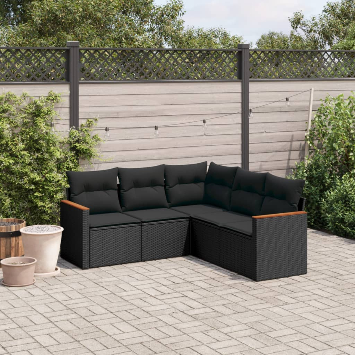 Schwarzes Korbmöbel mit schwarzen Kissen. In einem Garten mit Zaun und Pflanzen.