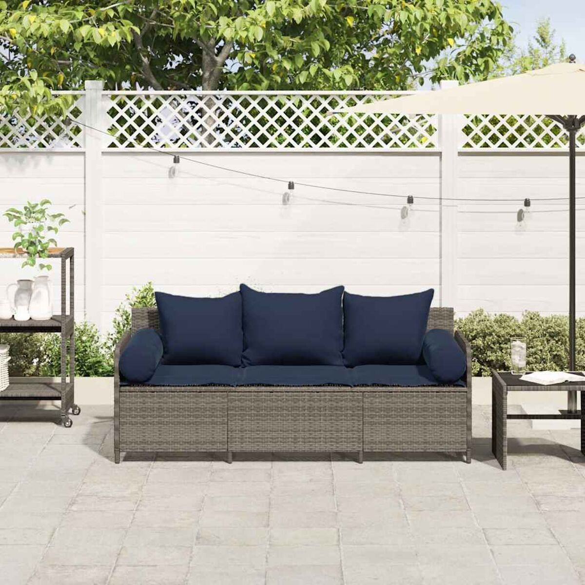 Divano in rattan con cuscini blu, su un patio. Recinto bianco e verde sullo sfondo.
