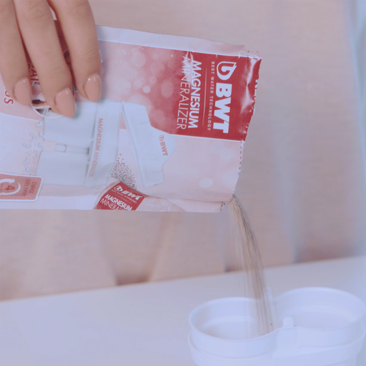 Ręka wlewa mineralizator magnezu do przezroczystej szklanki. Widoczne opakowanie produktu.