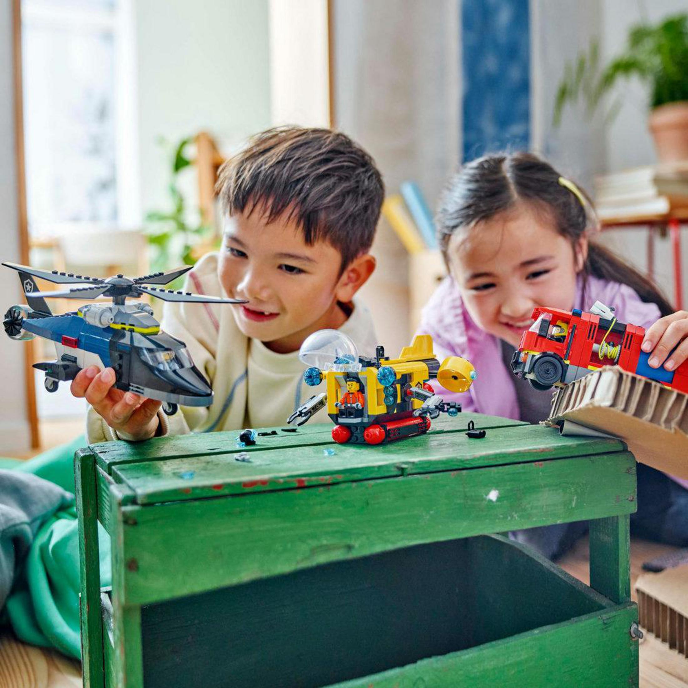 Dos niños jugando con juguetes de rescate de bomberos y helicópteros LEGO en una mesa verde.