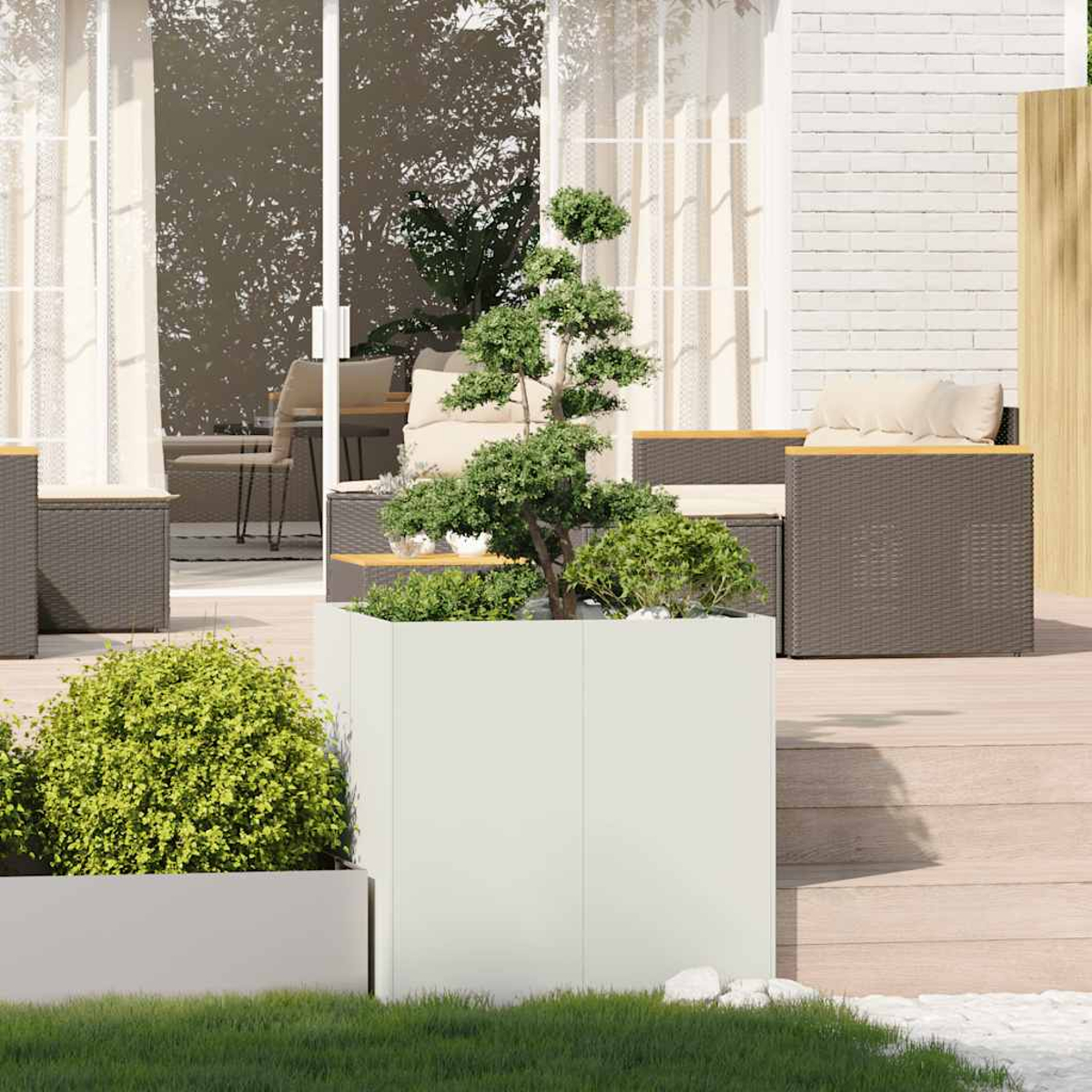 Fioriera bianca con un piccolo albero e altre piante, su un terrazzo in legno, con uno sfondo giardino.
