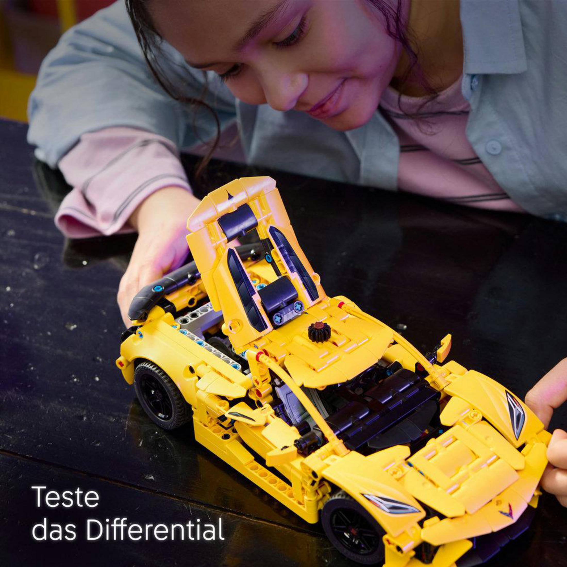 Un niño jugando con un coche modelo Lego Corvette amarillo. El capó está abierto.
