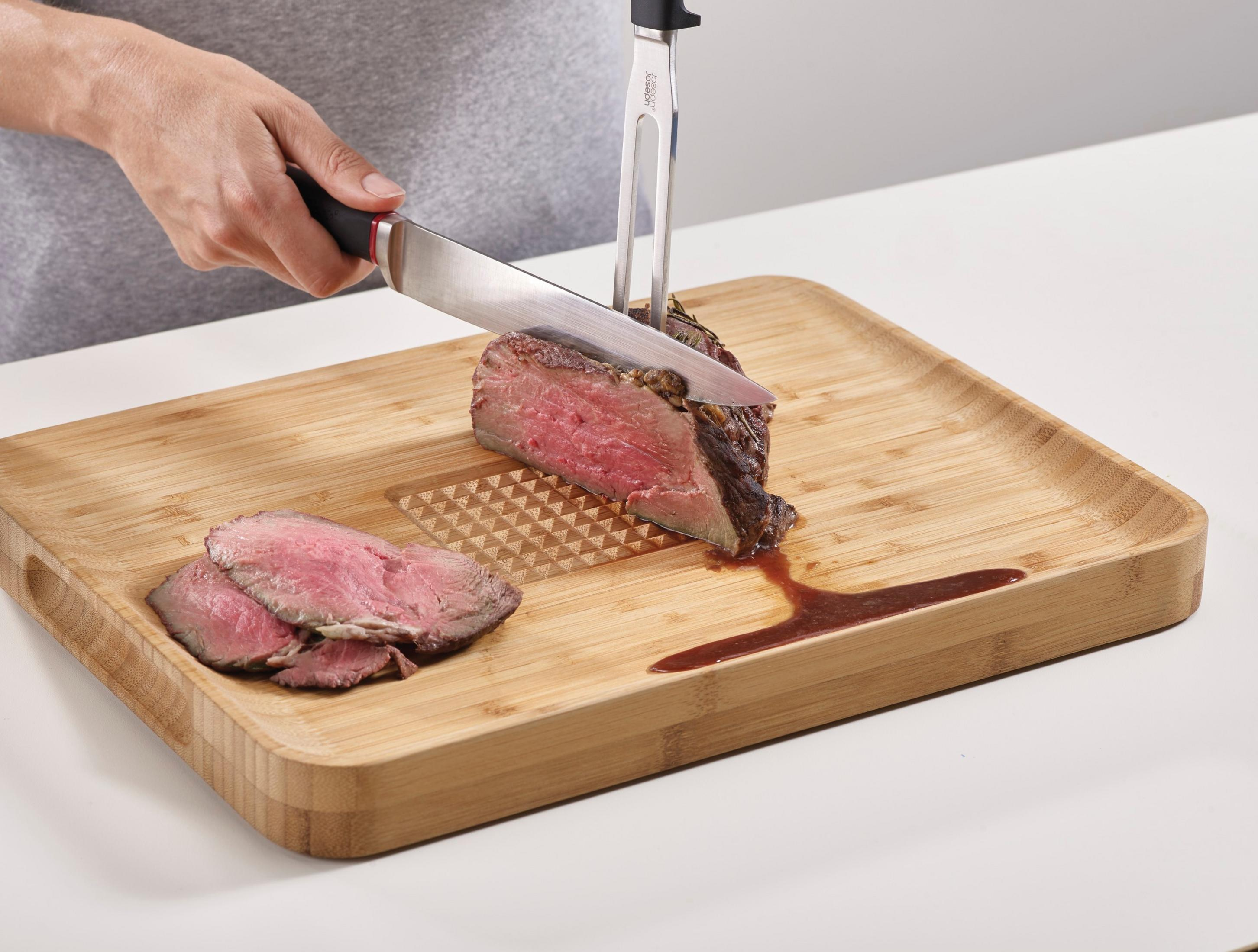 Person schneidet Roastbeef auf einem Bambus-Schneidebrett. Auf dem Brett befinden sich geschnittenes Rindfleisch und Soße.
