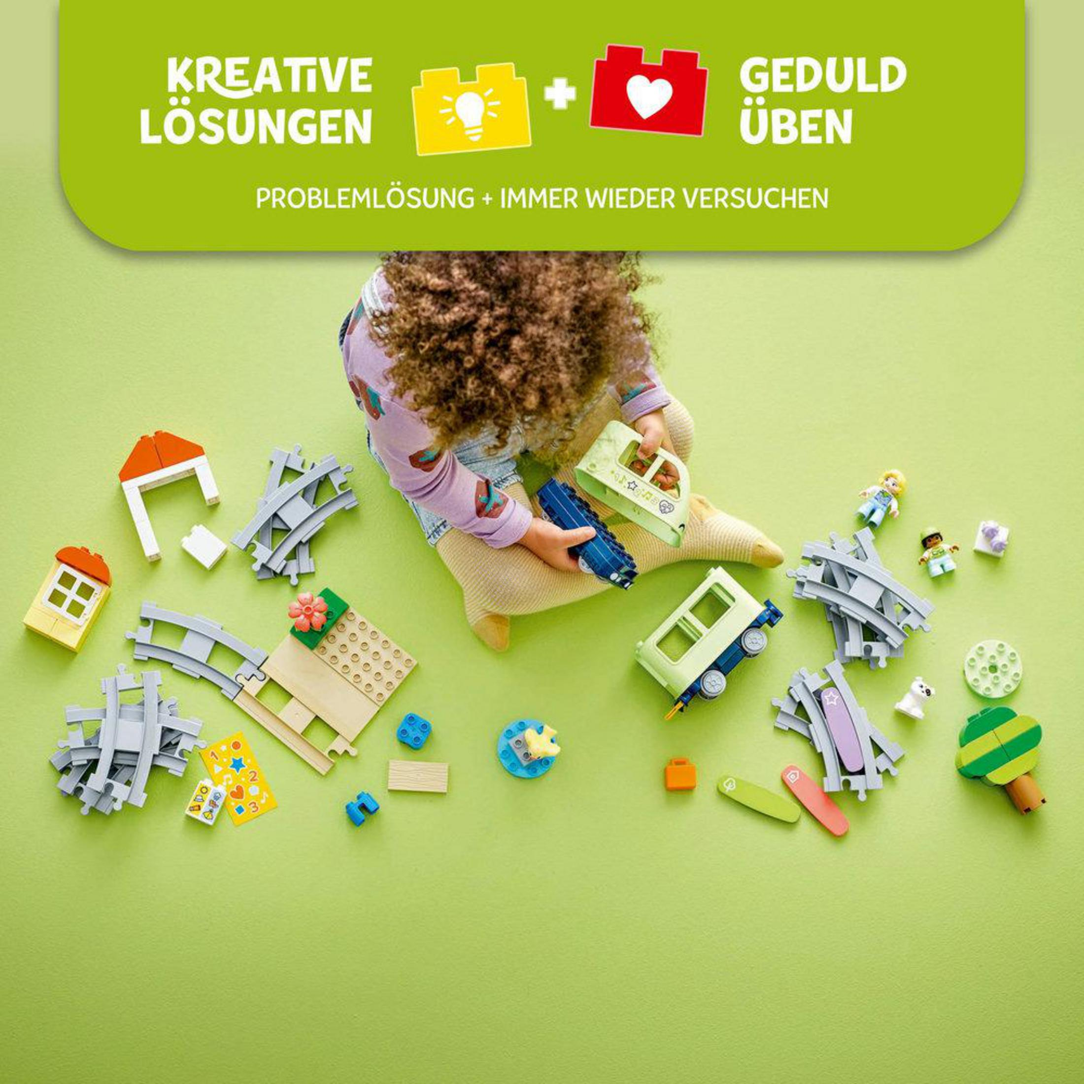 Widok dziecka na zestaw Lego Duplo z pociągiem, torami, figurkami i klockami. Elementy są rozrzucone.