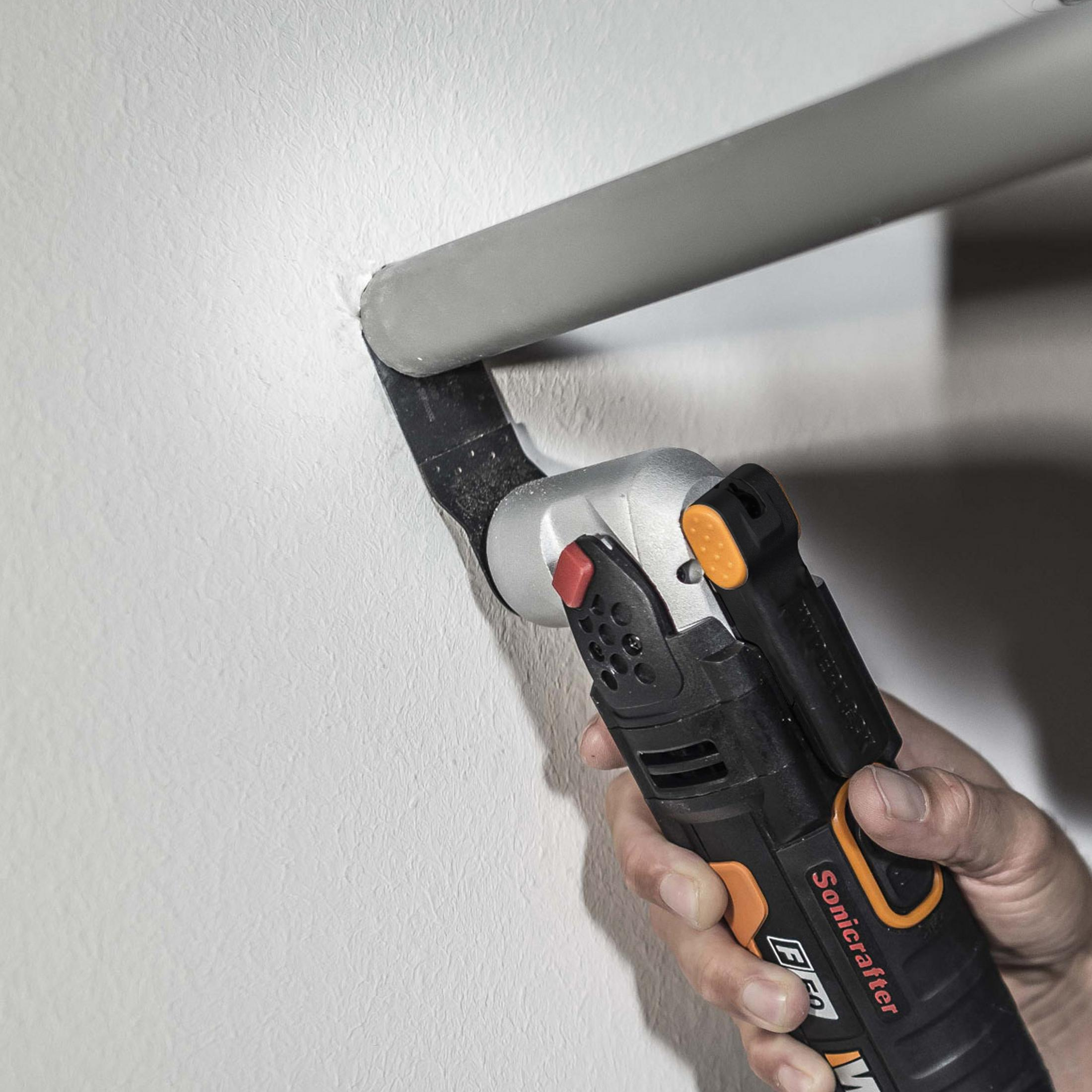 Ręka trzymająca czarno-srebrne narzędzie Sonicrafter, tnąca ścianę.