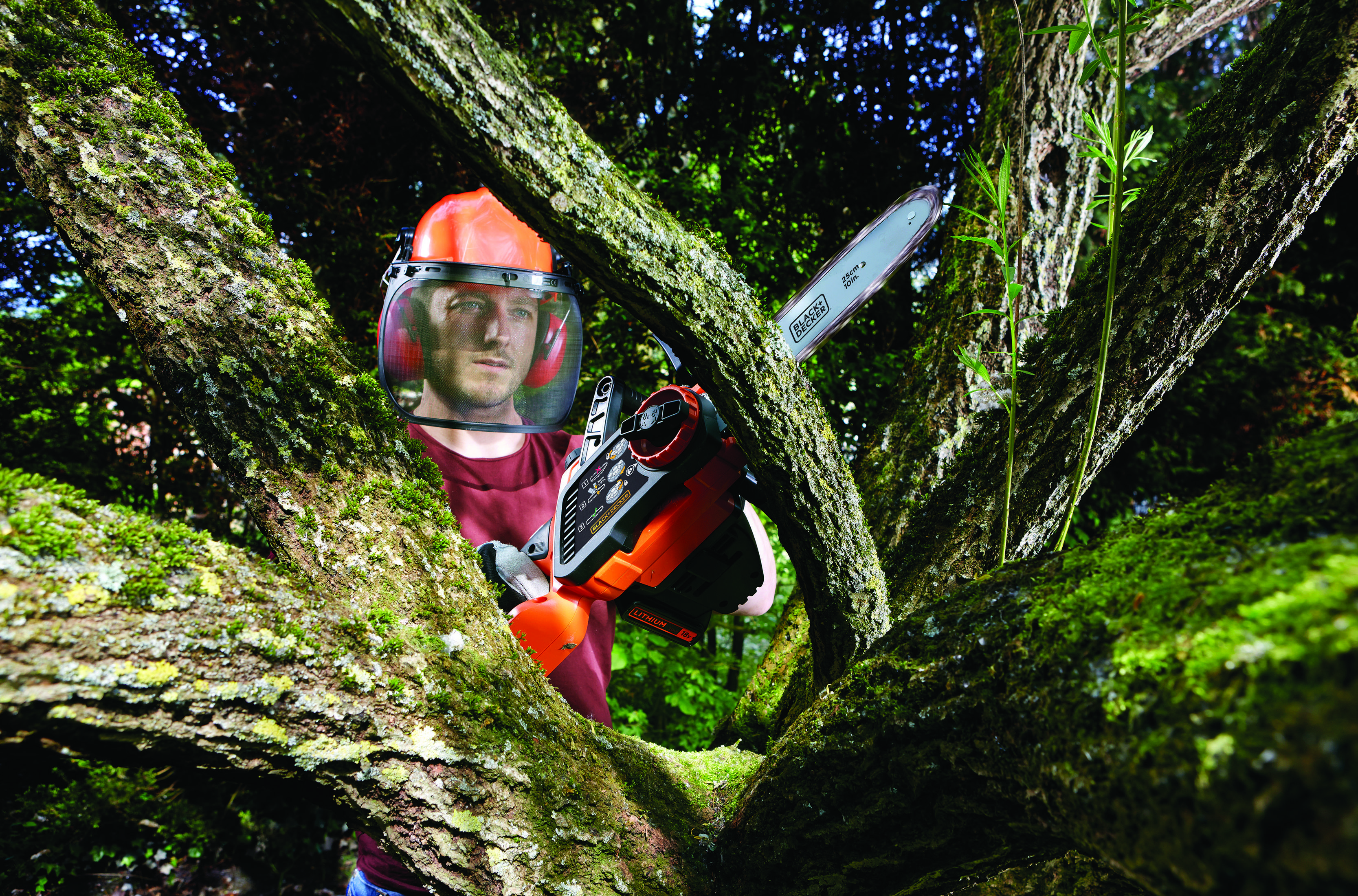 Mężczyzna w osłonie twarzy używa piły łańcuchowej w drzewie.