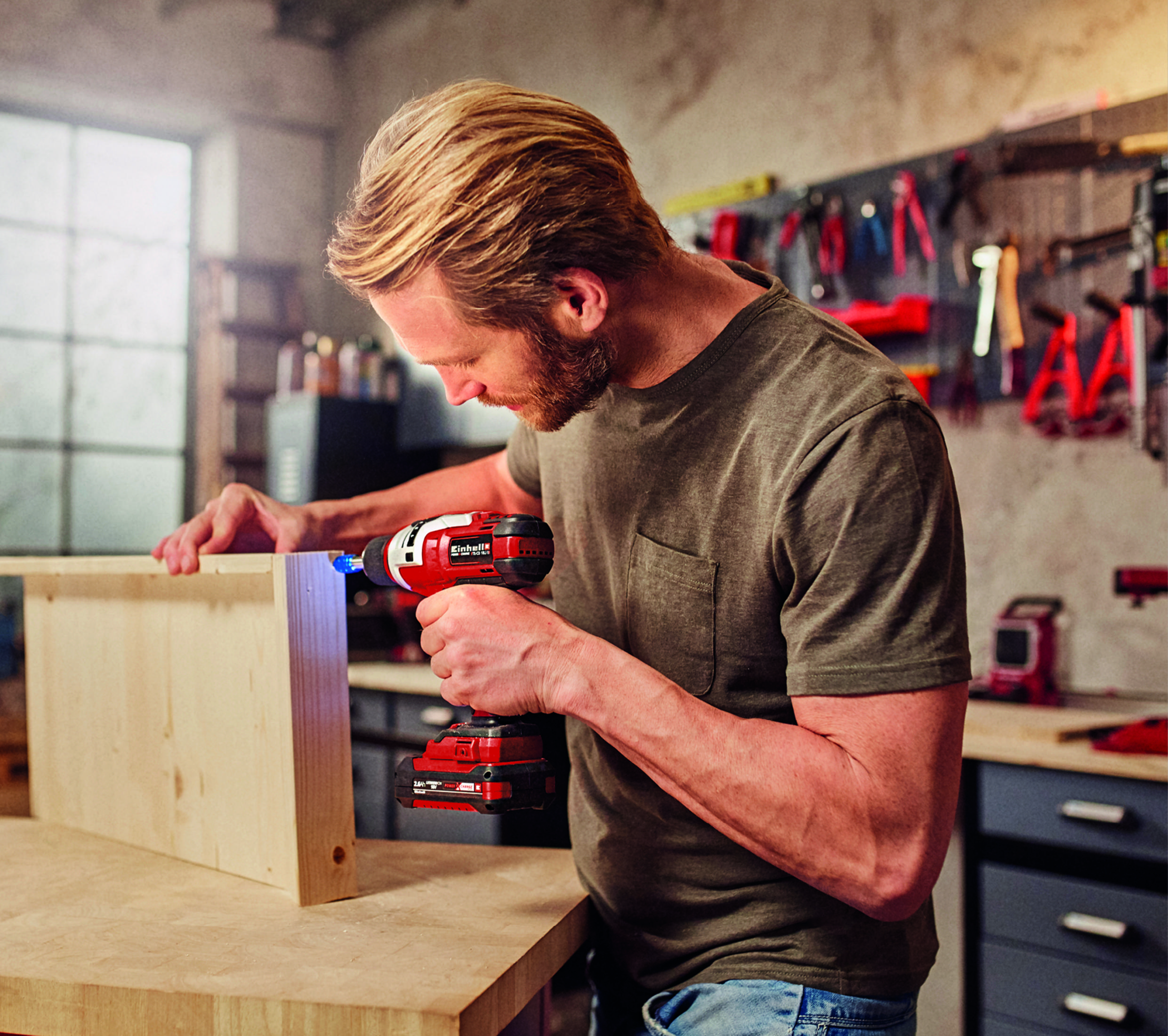 Mężczyzna używa czerwono-srebrnej wiertarki akumulatorowej do montażu drewnianej konstrukcji.