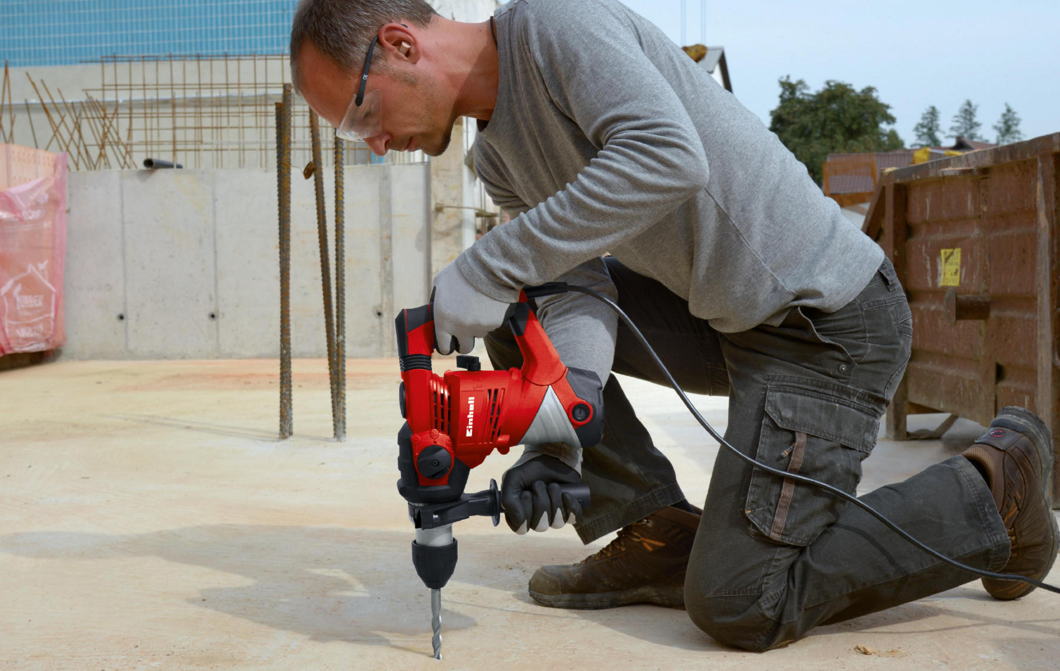 Un uomo fora il cemento con un trapano rosso mentre è in ginocchio in un cantiere.
