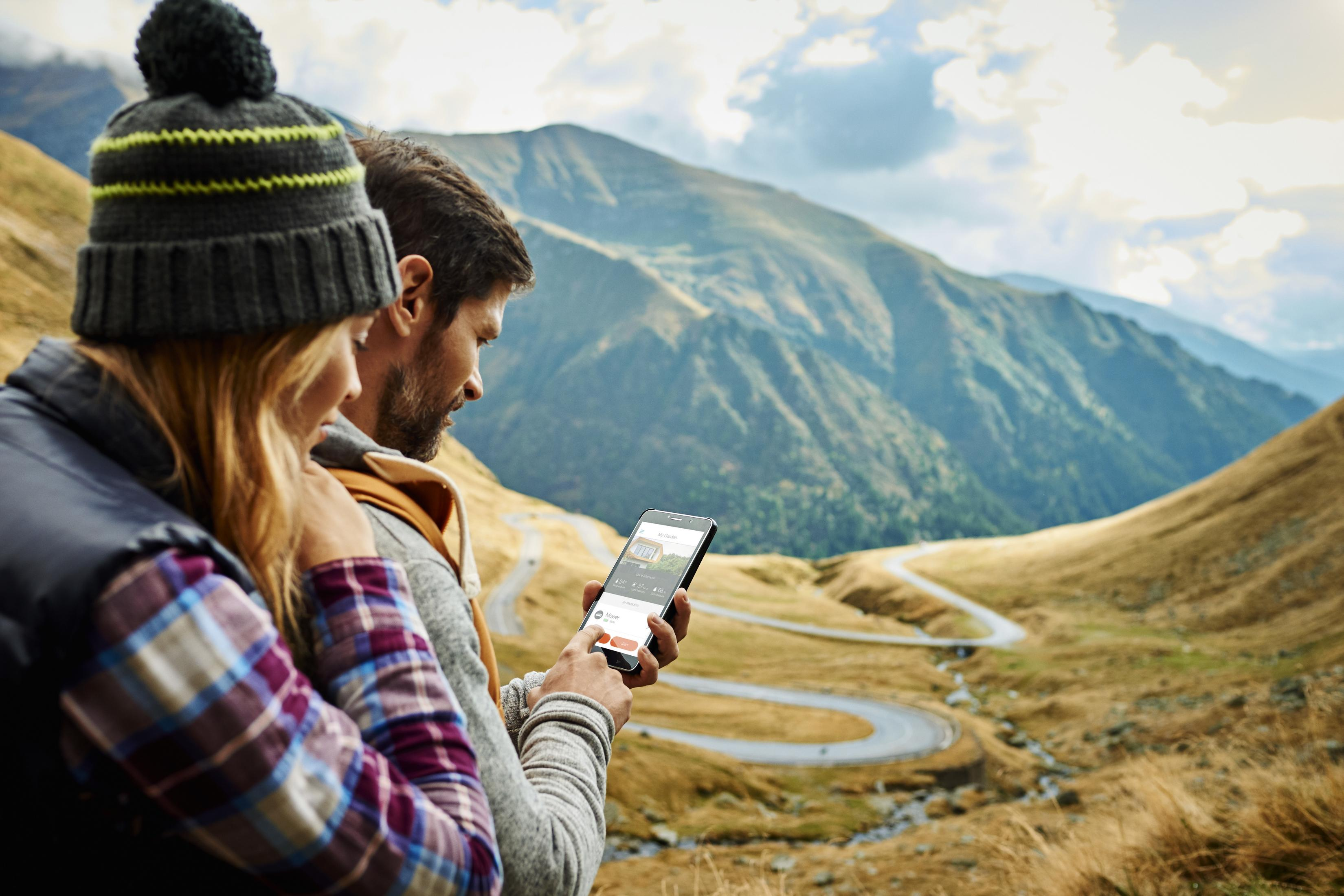 Paar benutzt Telefon zur Navigation in den Bergen. Malerische Serpentinenstraße im Hintergrund.