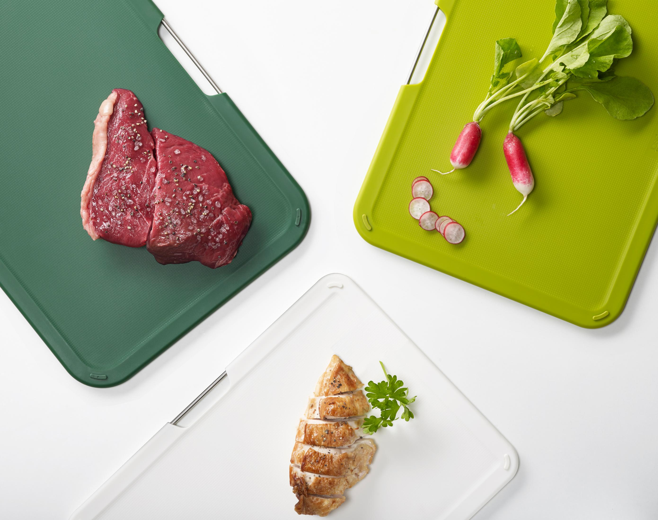 Tres tablas de cortar con comida: bistec en verde, rábanos en verde y pollo en rodajas en blanco.