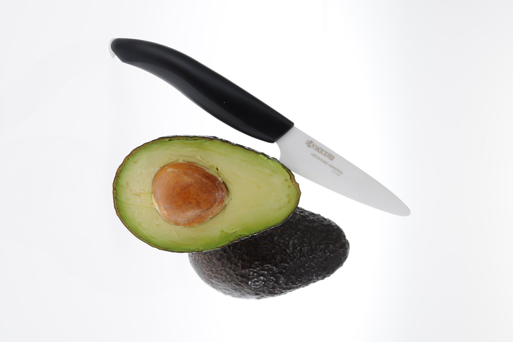 In zwei Hälften geschnittene Avocado mit Messer auf weißem Hintergrund.