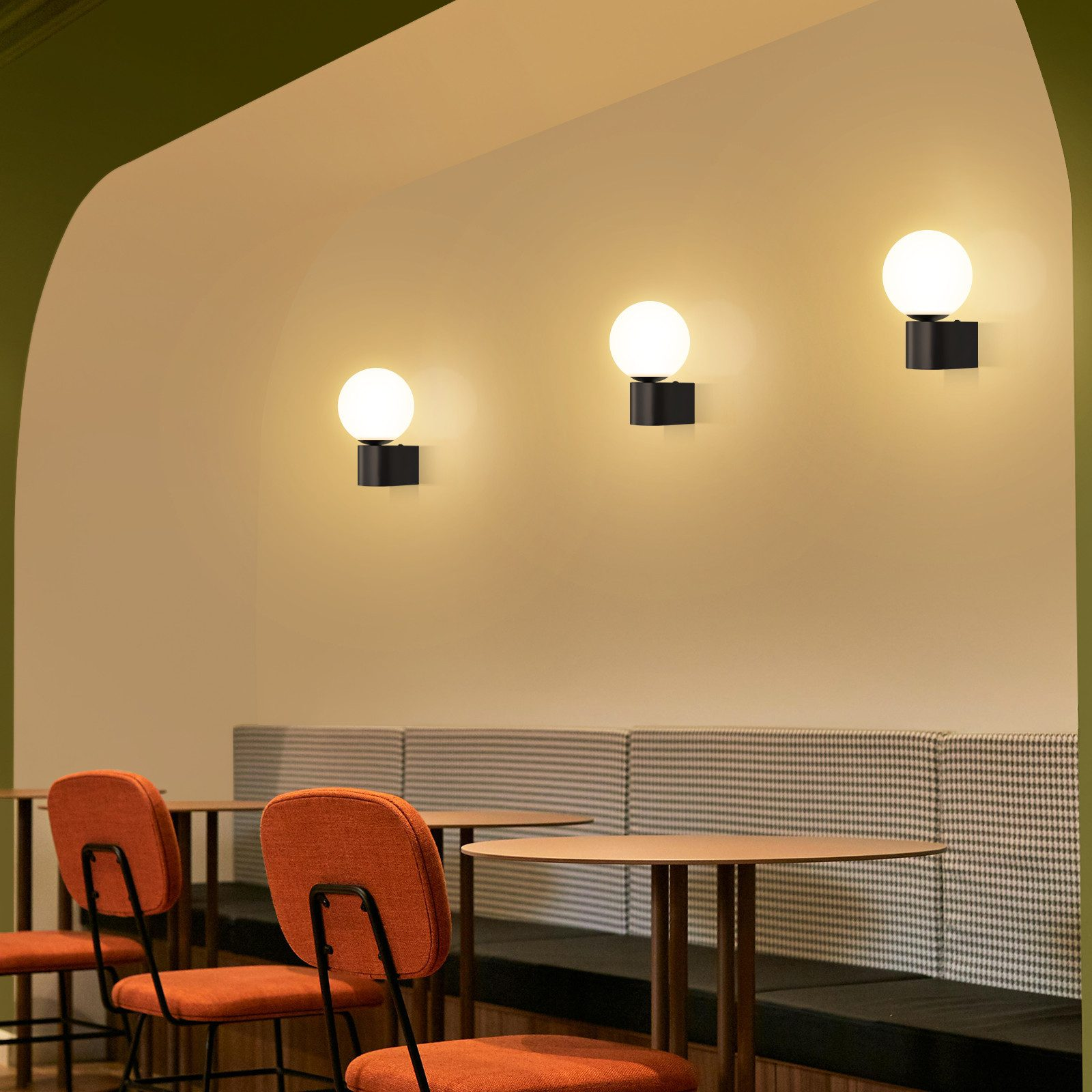 Tre lampade nere con luci sferiche bianche su un muro in un ambiente da caffè.