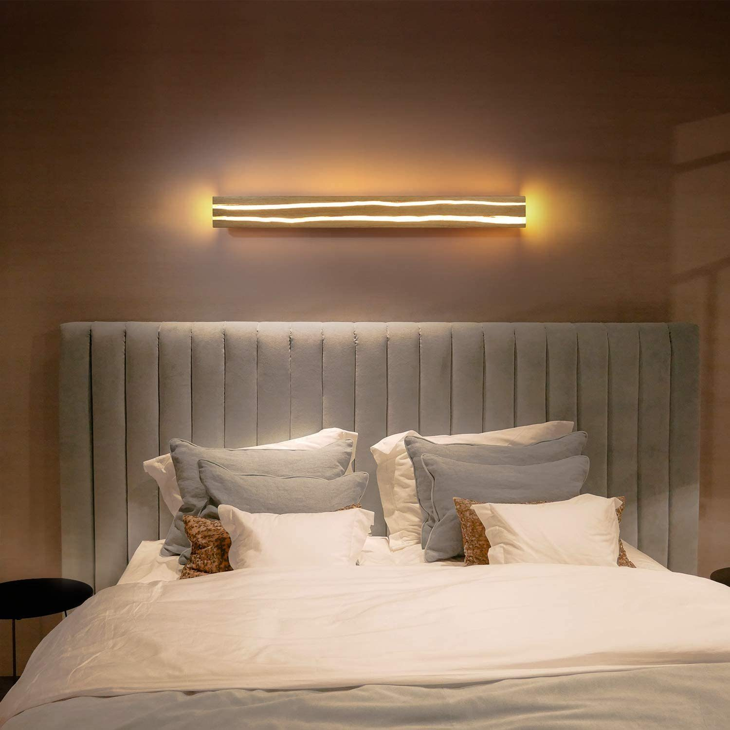 Lampada da parete in legno con tre linee luminose, sopra un letto.