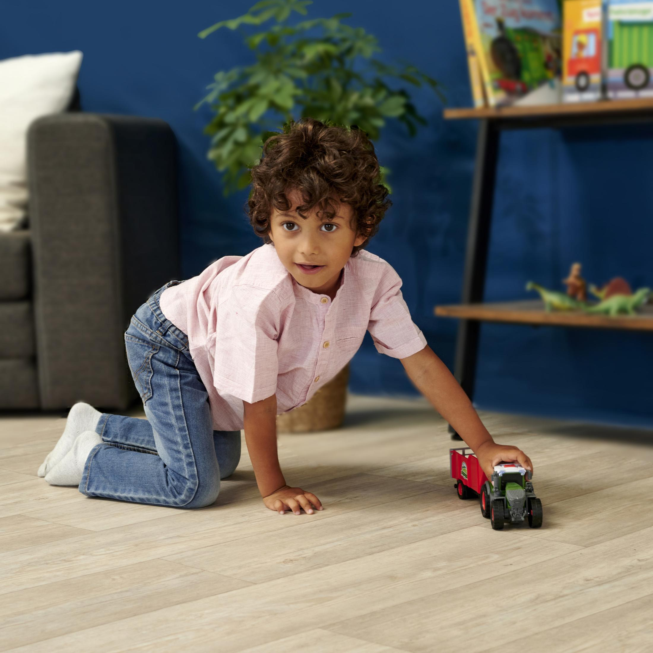 Mały chłopiec na podłodze, bawiący się zabawką-traktorem i patrzący w kamerę.