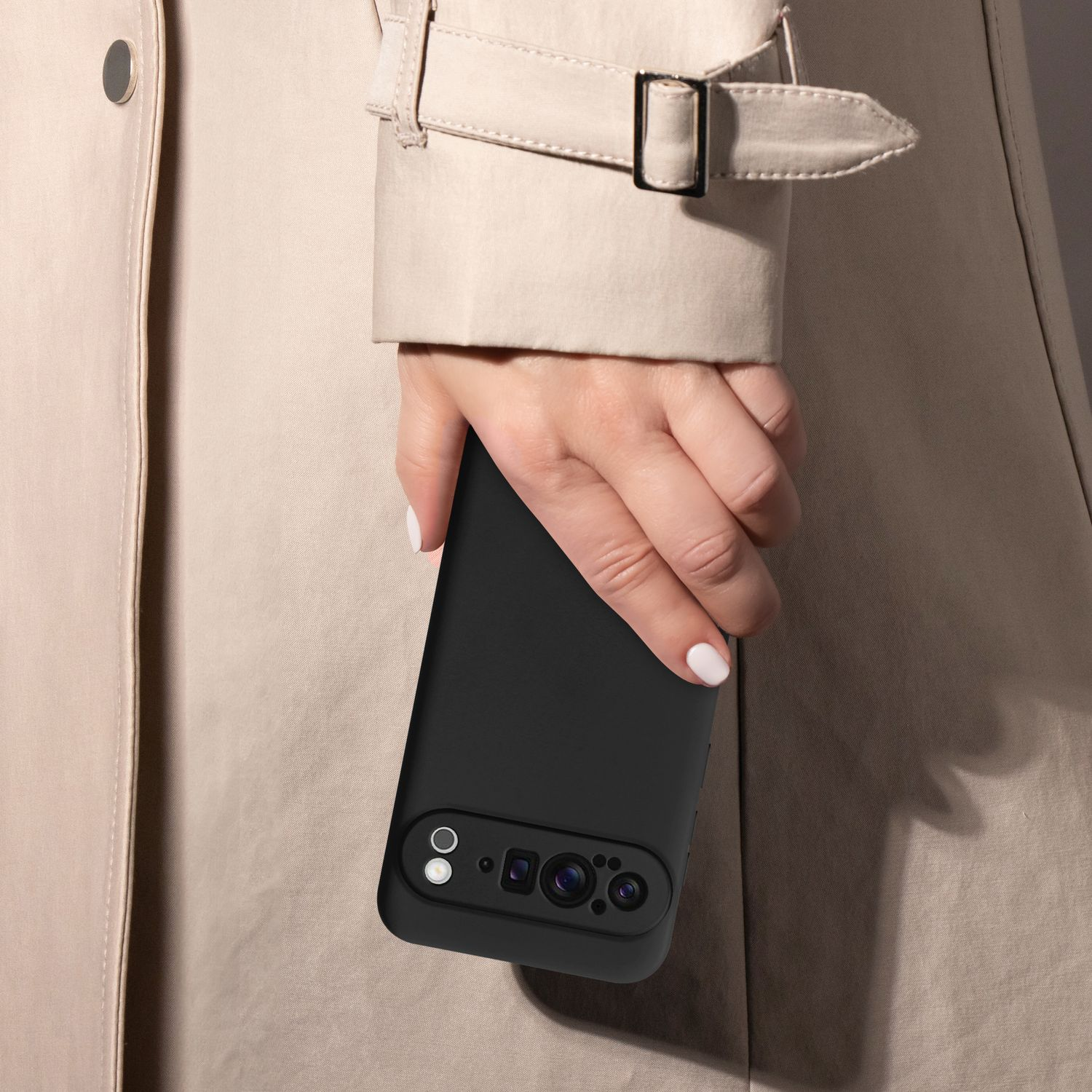 Eine Hand, die ein Telefon in einer schwarzen Hülle hält, trägt einen beigen Trenchcoat.