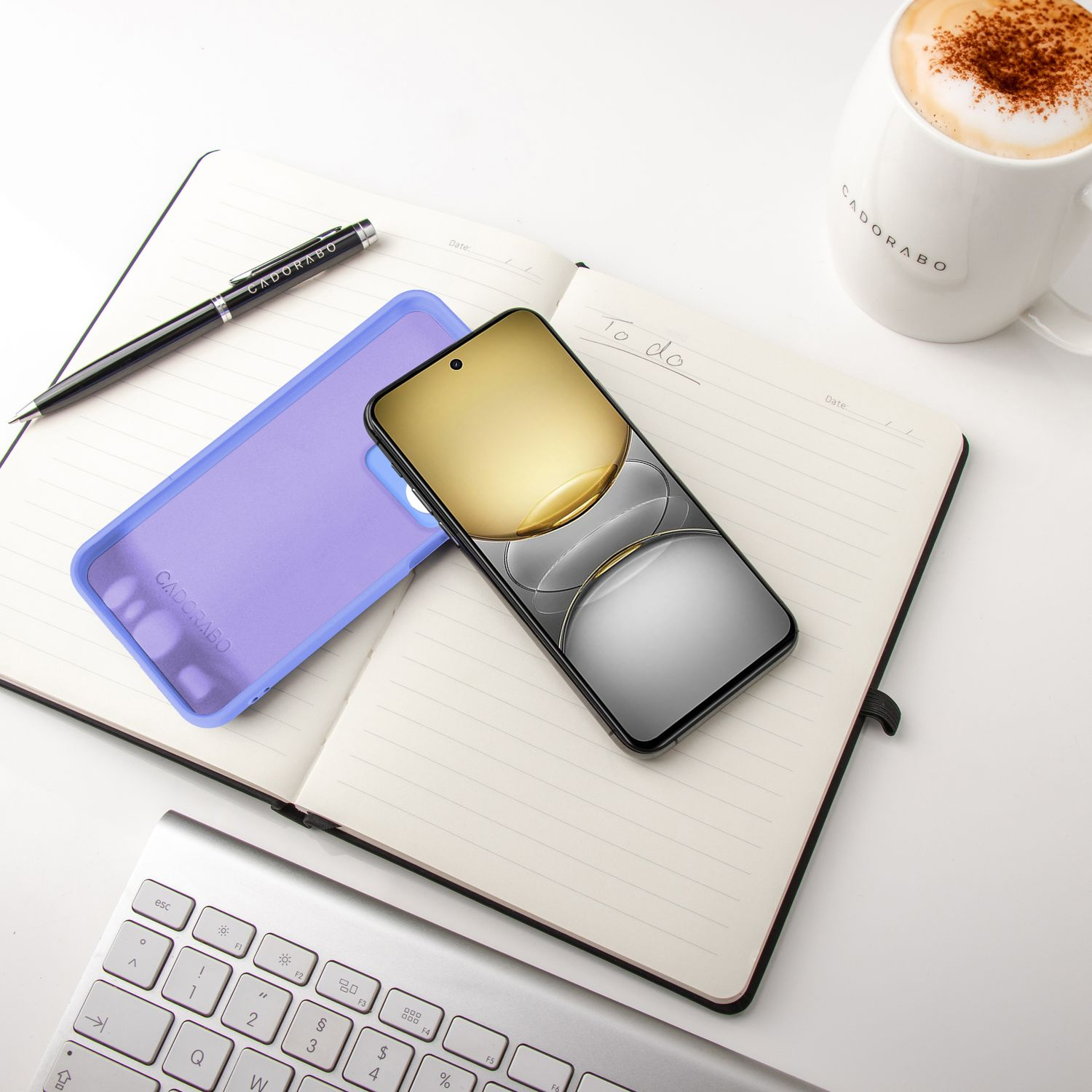 Ein Notizbuch, ein Stift, eine Handyhülle und ein Telefon auf einem weißen Schreibtisch.