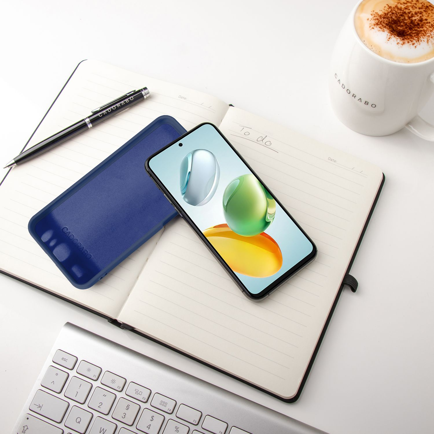 Telefon auf offenem Notizbuch mit Stift und Kaffee. Blaue Handyhülle neben dem Telefon.