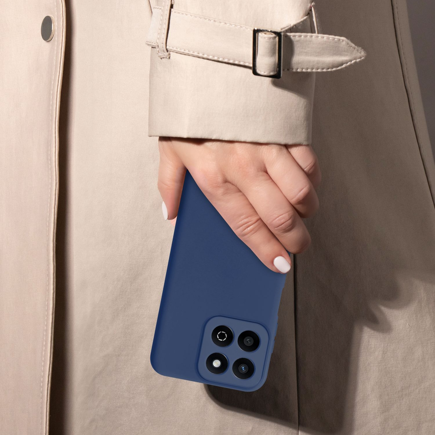 Die Hand einer Frau hält ein dunkelblaues Telefon vor dem Hintergrund eines beigen Trenchcoats.