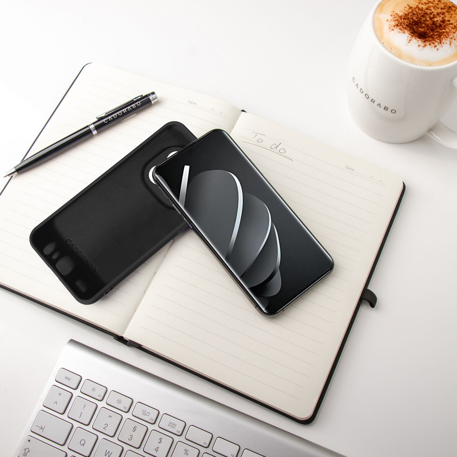 Notizbuch mit Telefon, Hülle, Stift und Kaffee. Weiße Oberfläche.