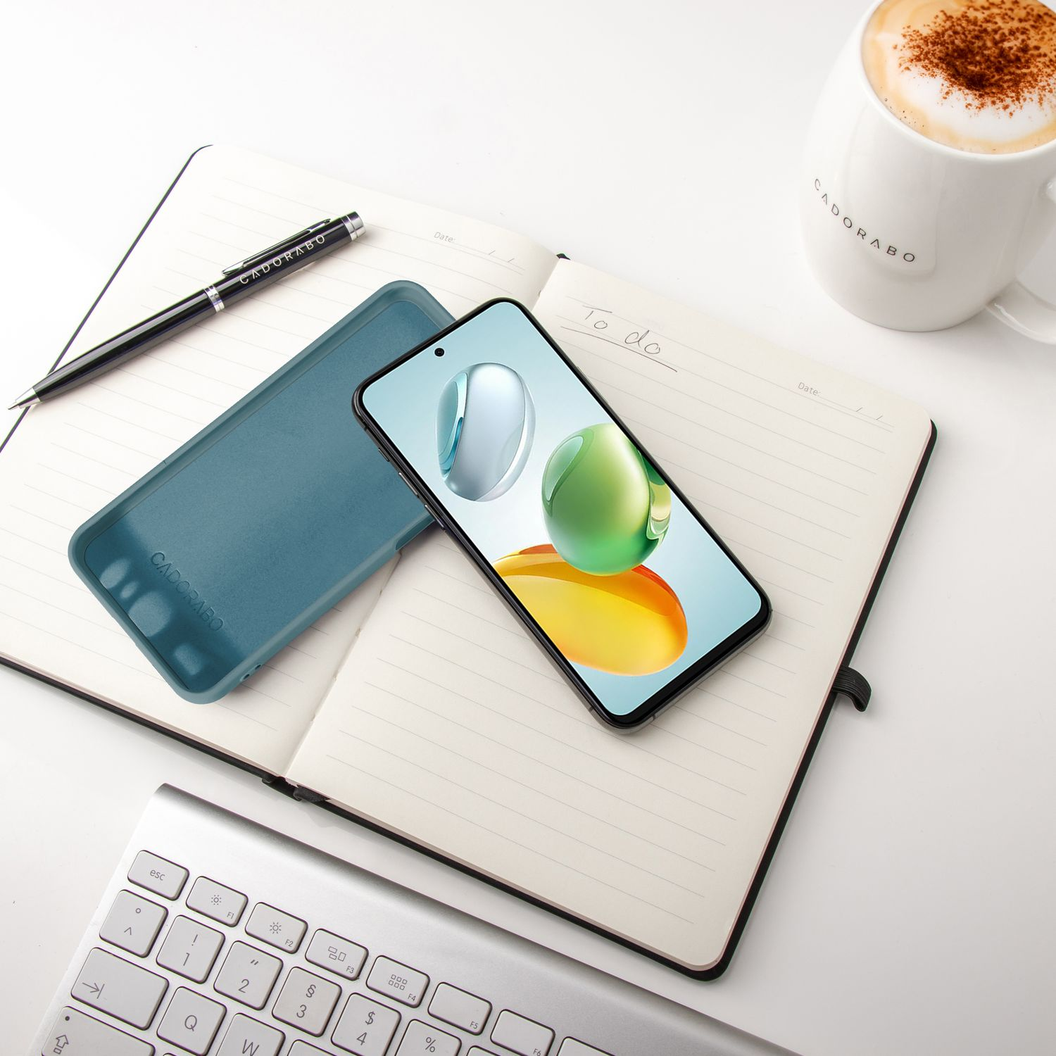 Telefon und Hülle auf einem Notizbuch mit Stift und Kaffeetasse. Weißer Schreibtisch und Hintergrund.