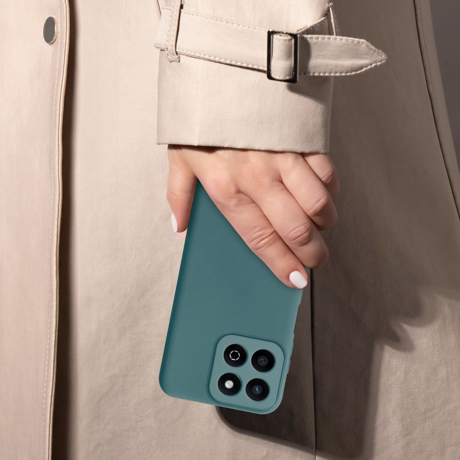 Frau hält ein türkisfarbenes Telefon mit Kamera. Beiger Trenchcoat-Hintergrund. Weiße Nägel.