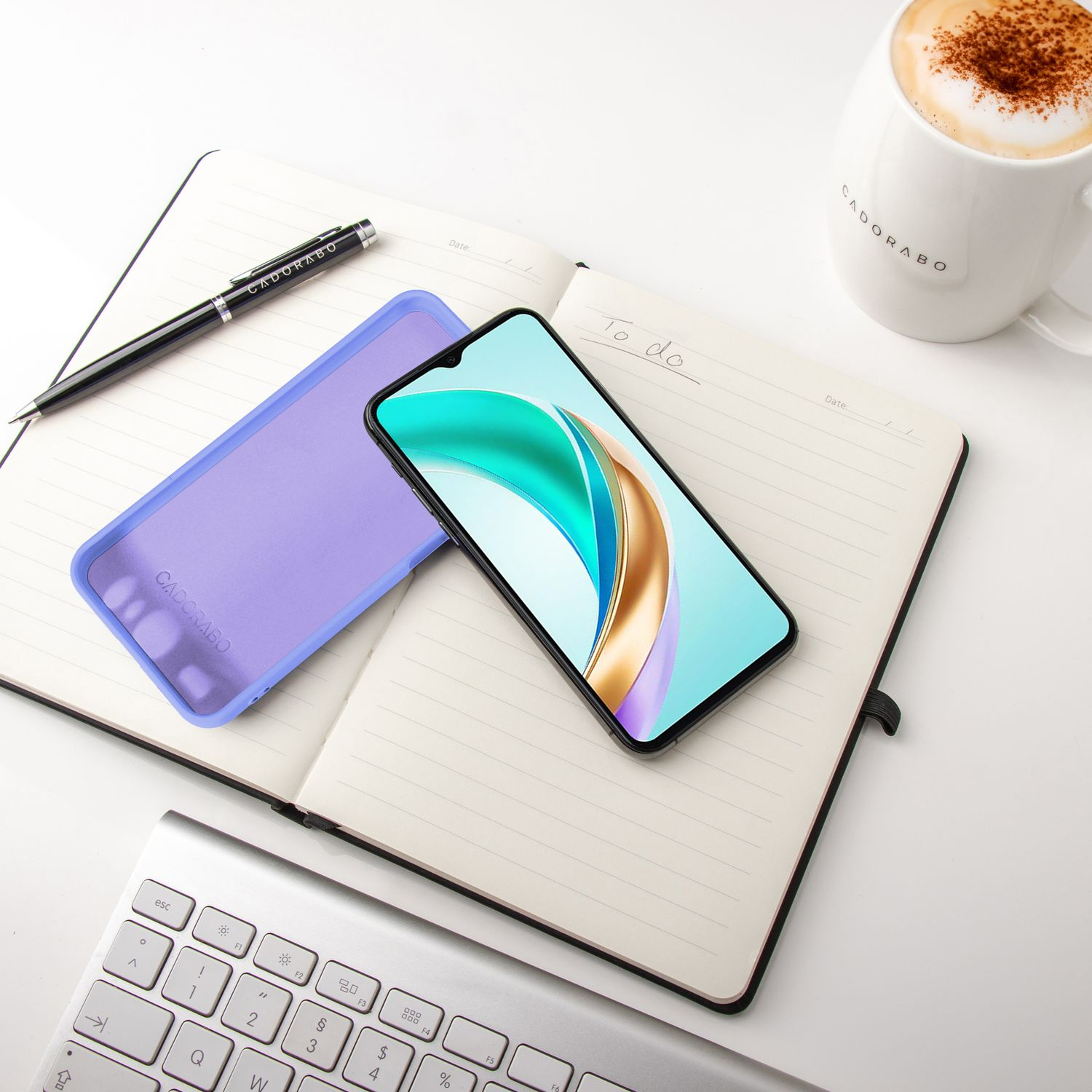 Notizbuch mit Telefon und Hülle, Stift und Kaffeetasse auf weißem Schreibtisch.