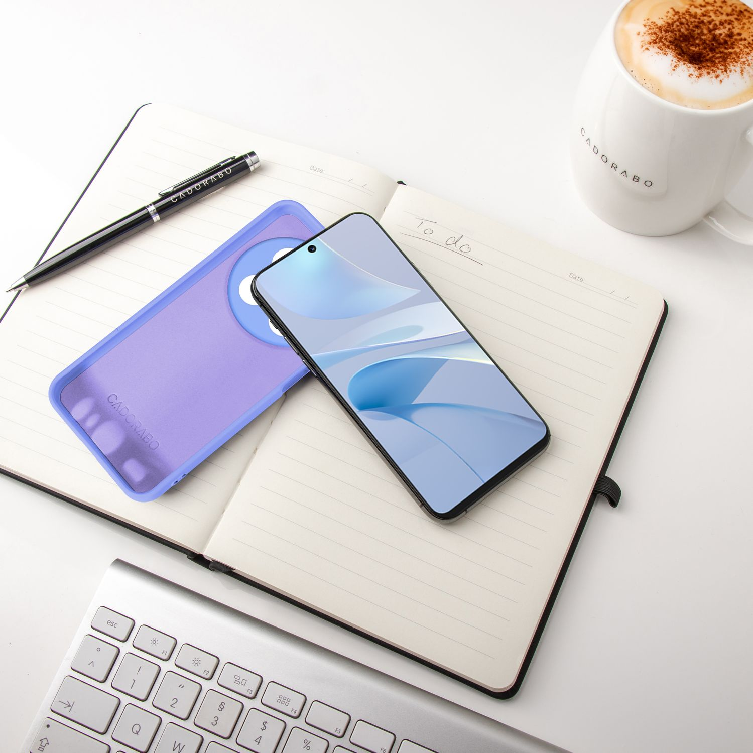 Notizbuch geöffnet, mit Telefon und Hülle, Stift und Kaffeetasse. Weißer Hintergrund.