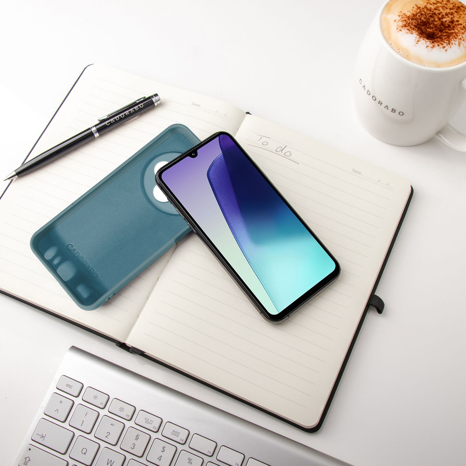 Notizbuch mit Telefon, Hülle, Stift und Kaffee. Weiße Oberfläche.