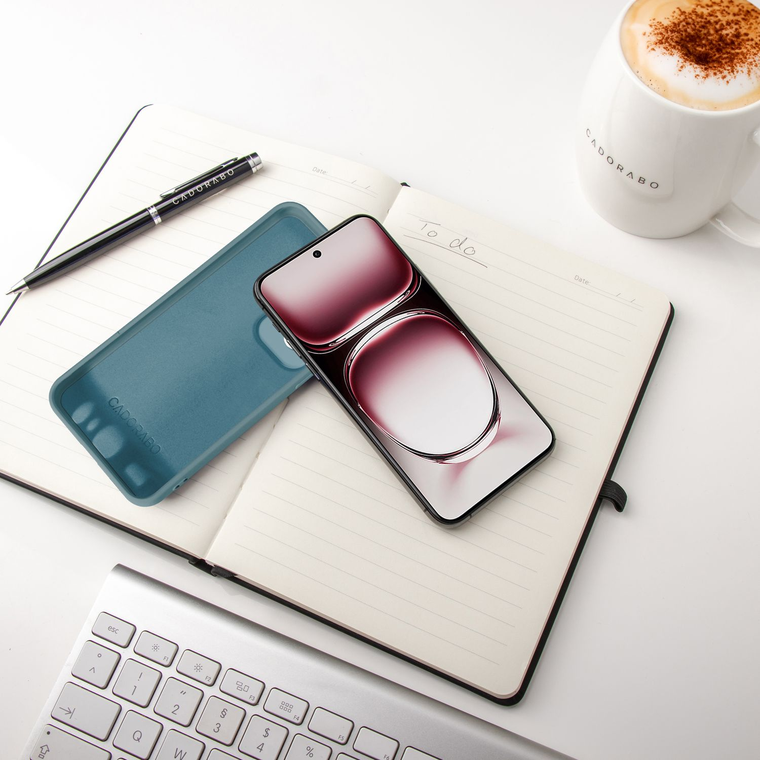 Telefon und Hülle auf einem Notizbuch mit Stift und Kaffee. Tastatur im Hintergrund.