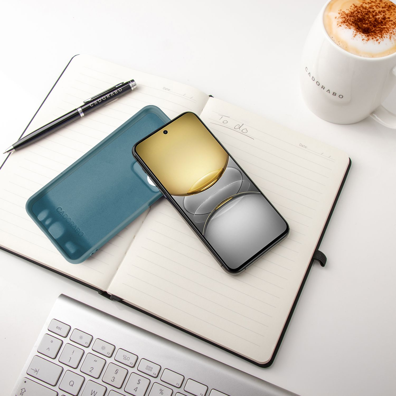 Notizbuch, Telefon, Hülle, Stift und Kaffeetasse auf weißem Schreibtisch. To-do-Liste sichtbar.