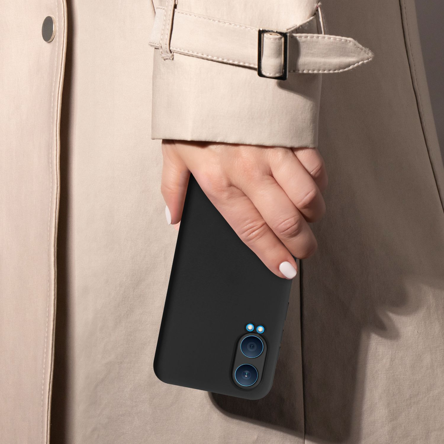 Hand hält schwarzes Telefon mit Hülle, trägt einen beigefarbenen Trenchcoat.