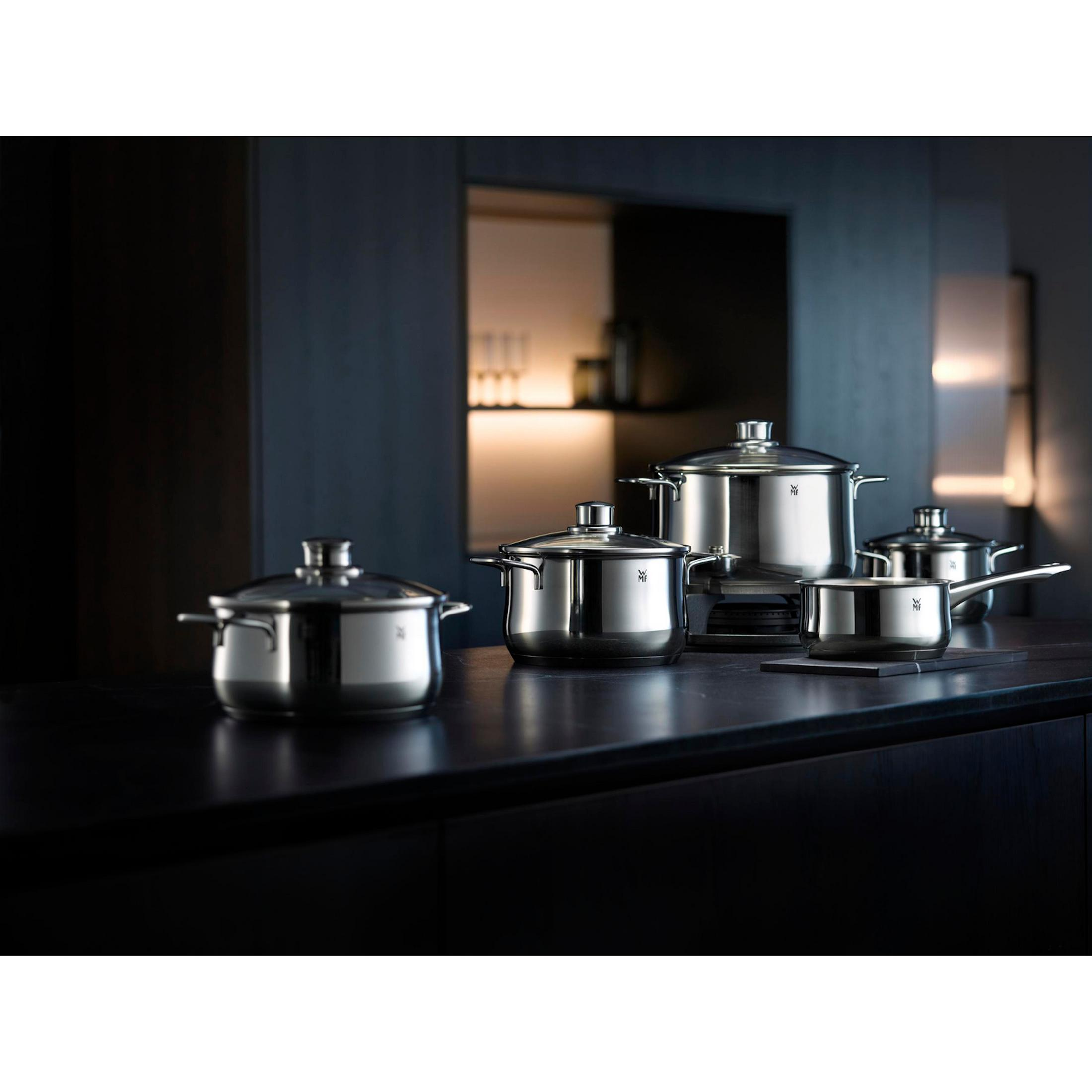 Casseroles en acier inoxydable sur un comptoir sombre. Fond sombre avec placards et lumières.