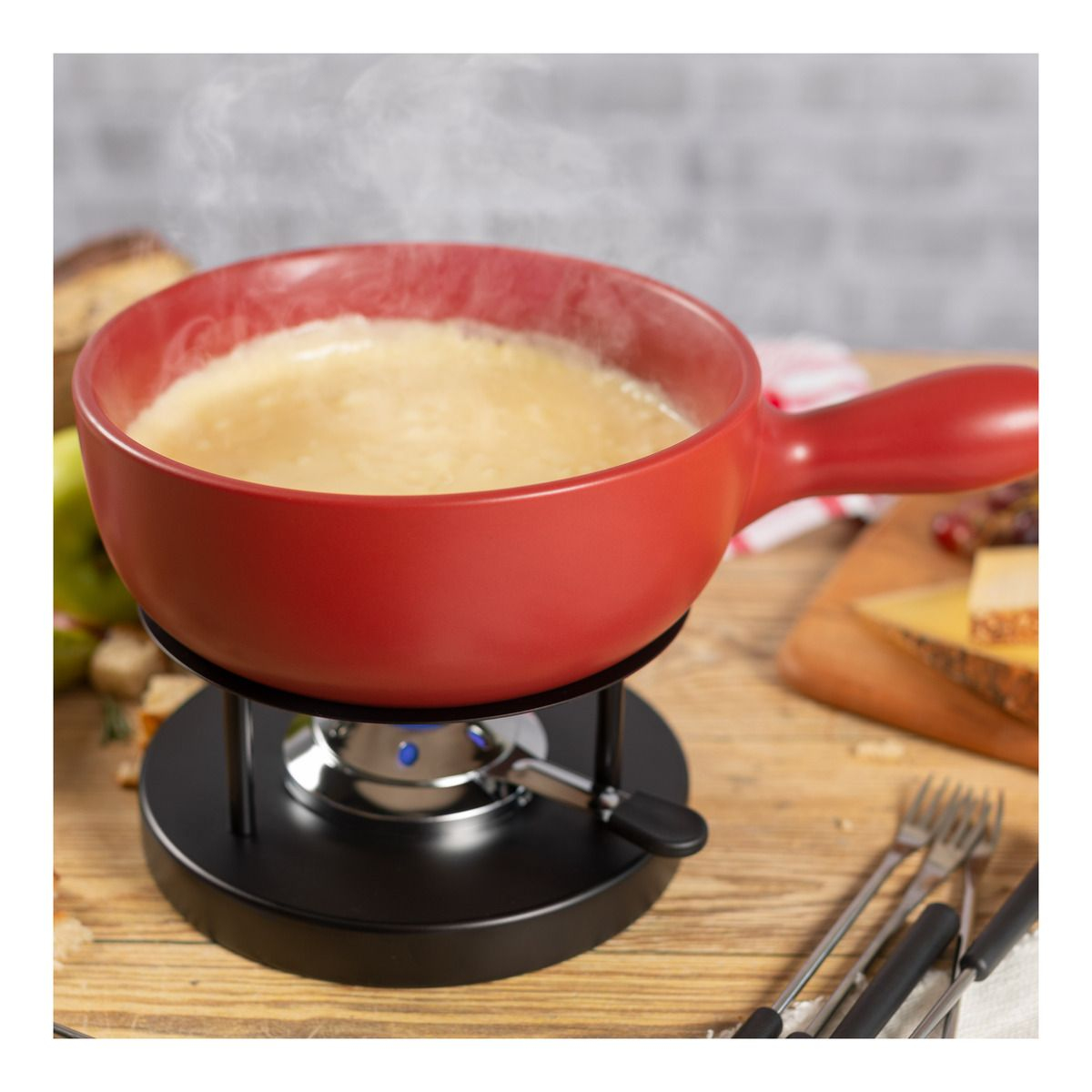 Roter Fonduetopf mit geschmolzenem Käse, Brot und Gabeln auf einem Holztisch.