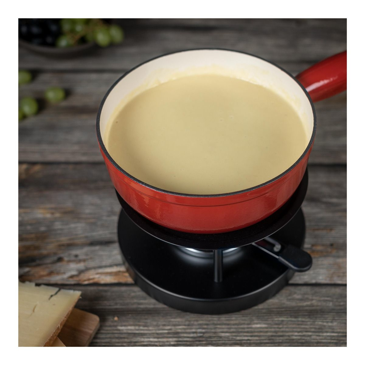Fondue-Topf mit geschmolzenem Käse, auf einem schwarzen Ständer und Holztisch.