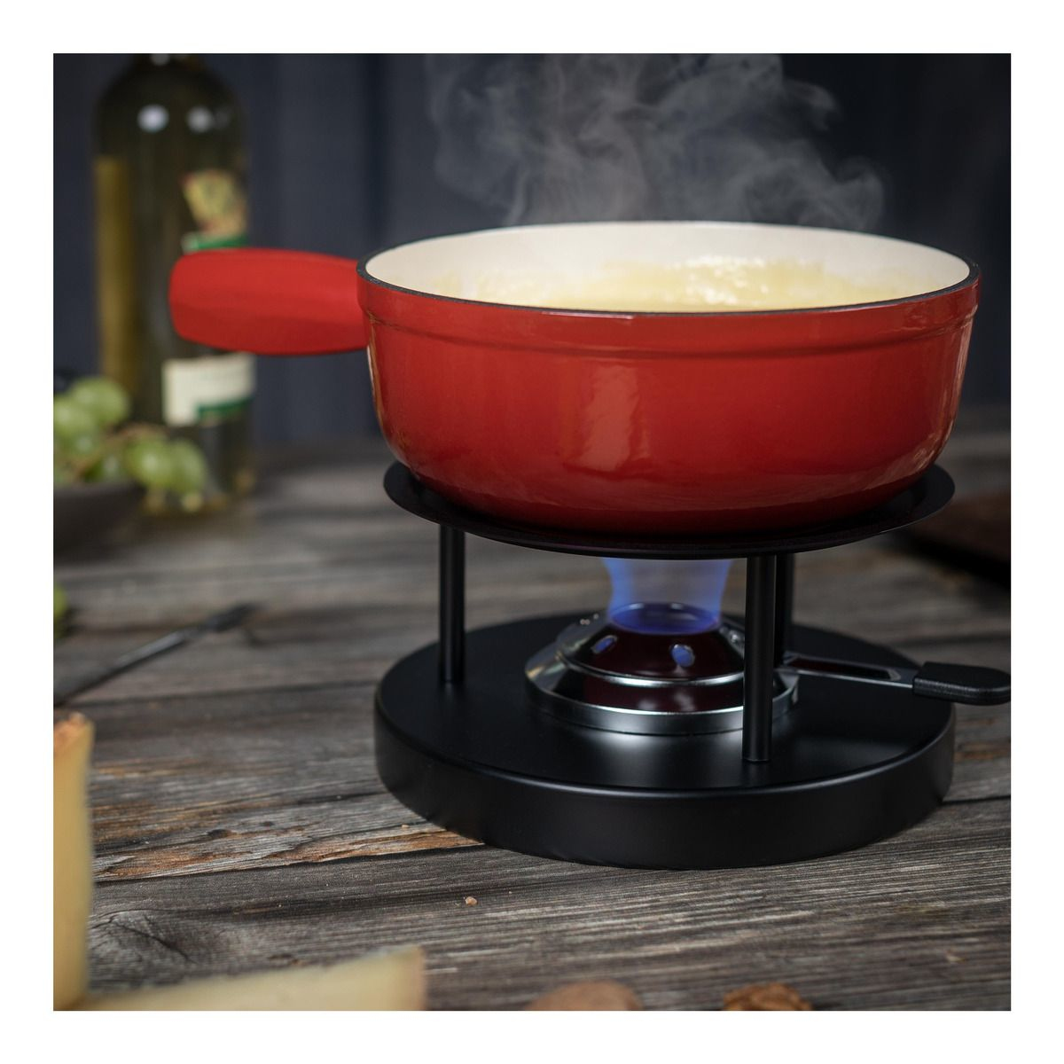 Roter Fonduetopf mit Dampf, auf schwarzem Ständer mit blauer Flamme, auf einem Holztisch.