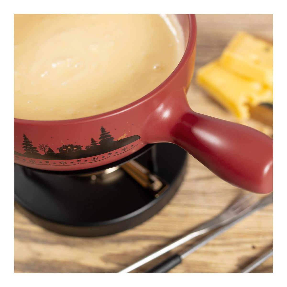 Ein roter Fonduetopf mit Käse, auf einem schwarzen Brenner, mit Käsescheiben und Gabeln drumherum.