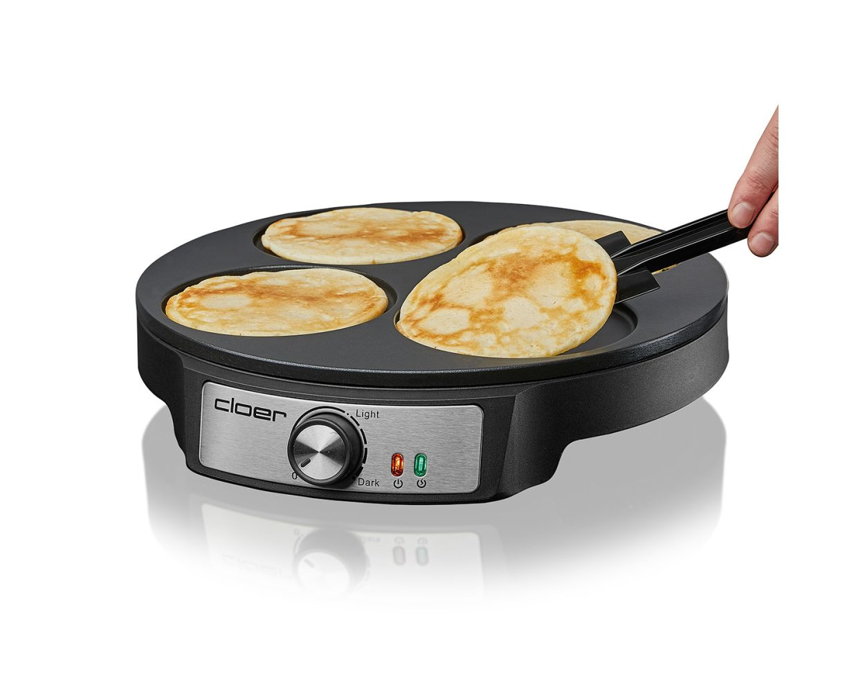 Macchina per pancake con quattro pancake, una mano che ne gira uno, su sfondo bianco.