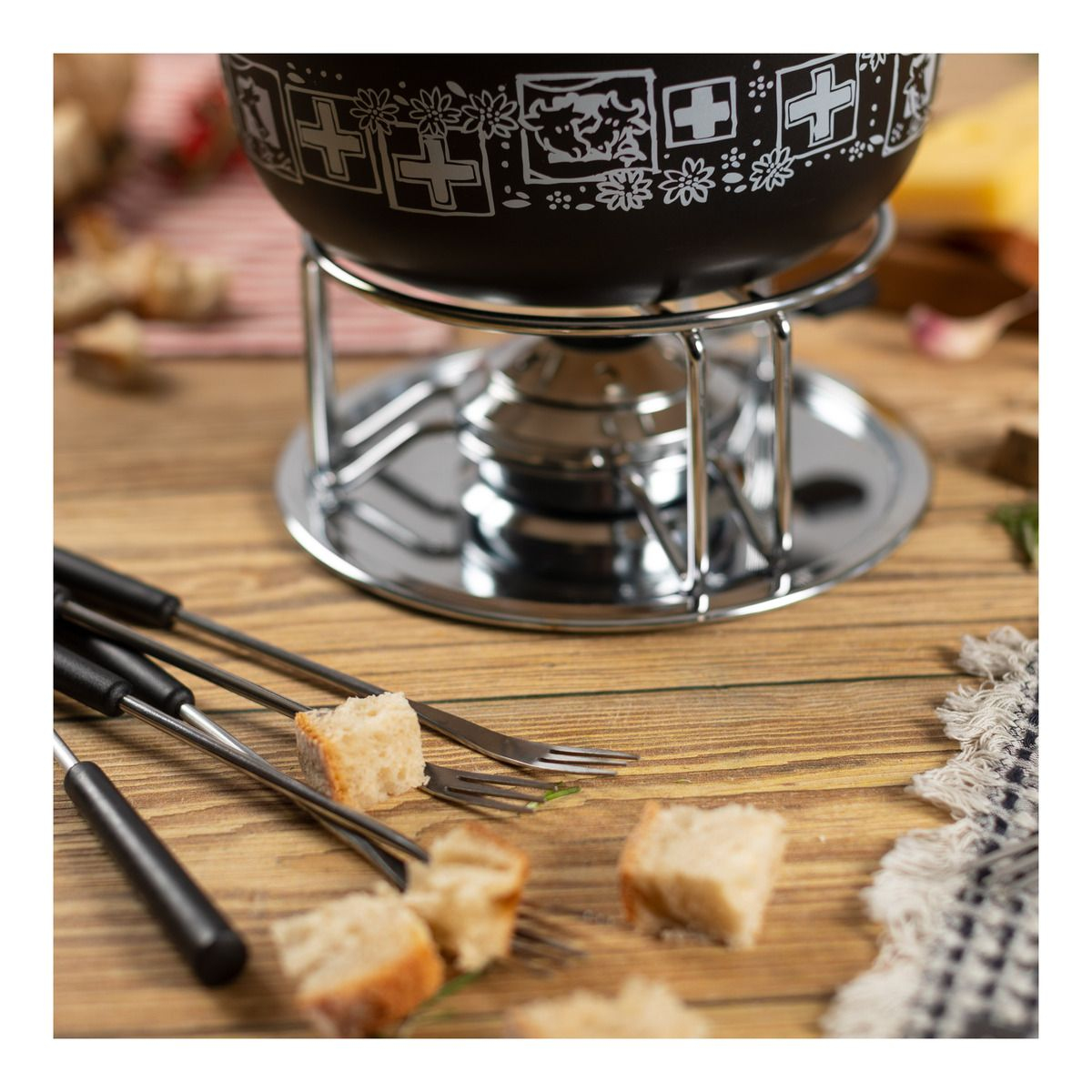 Ein schwarzes Fondue-Set mit Brotstücken auf Gabeln, auf einem Holztisch.