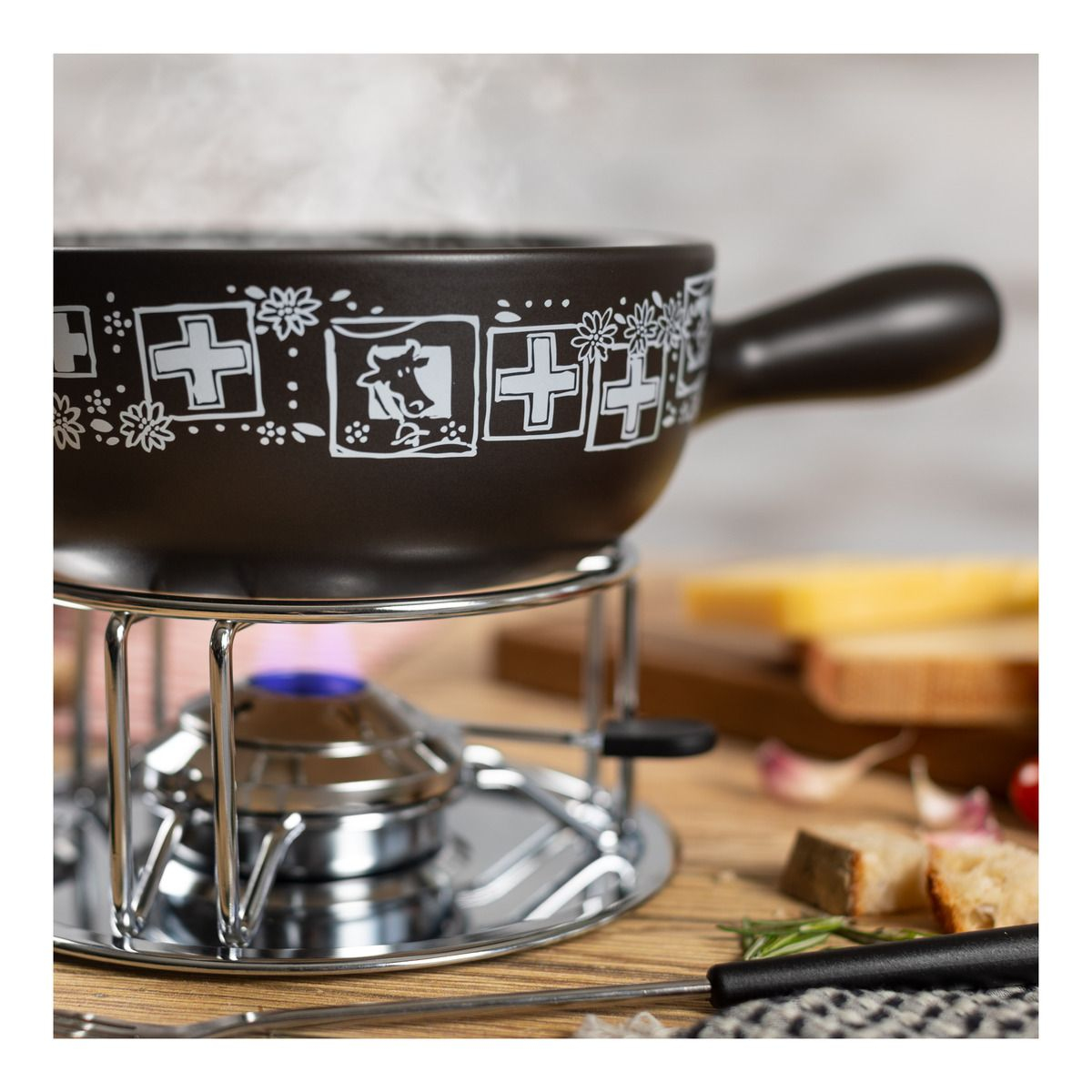 Fondue-Set mit dunkelbraunem Topf, silbernem Ständer und kleiner Flamme darunter.