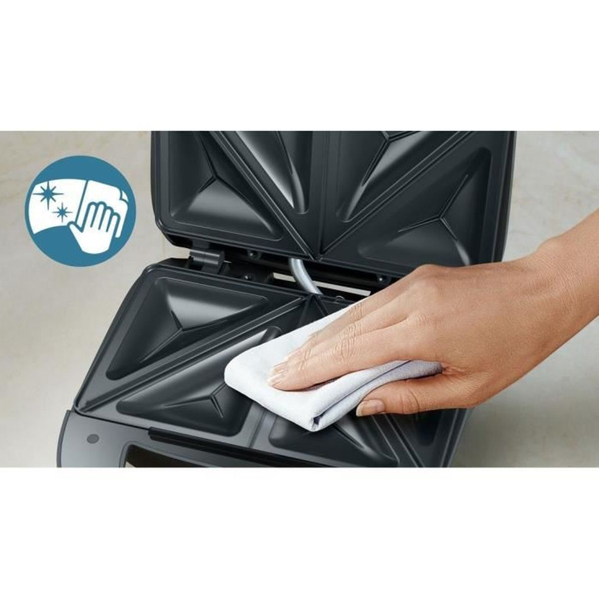 Ręka czyści opiekacz do kanapek. Opiekacz jest otwarty i czysty.