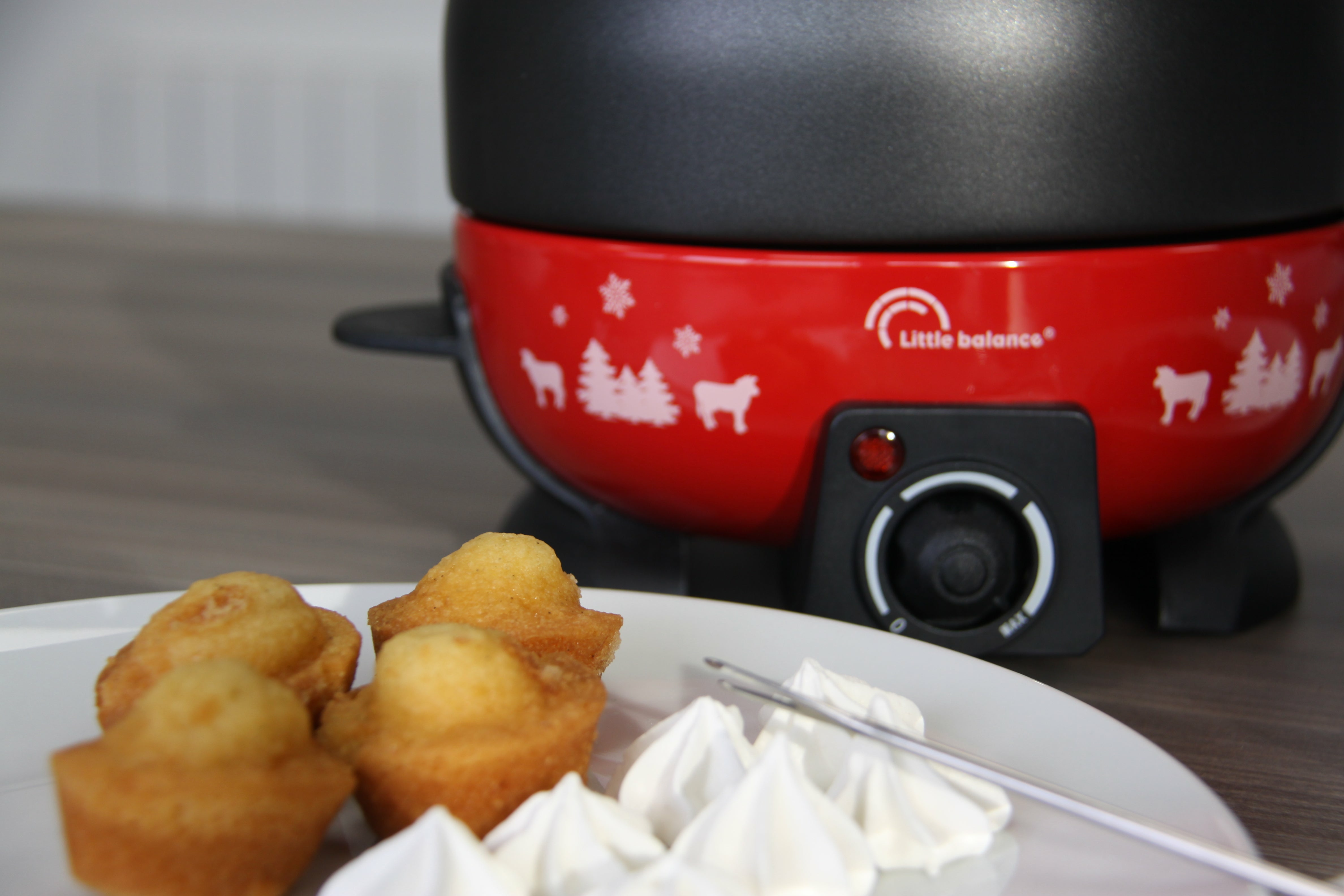 Roter Fonduetopf mit Essen auf einem weißen Teller, darunter kleine Kuchen und Baisers.