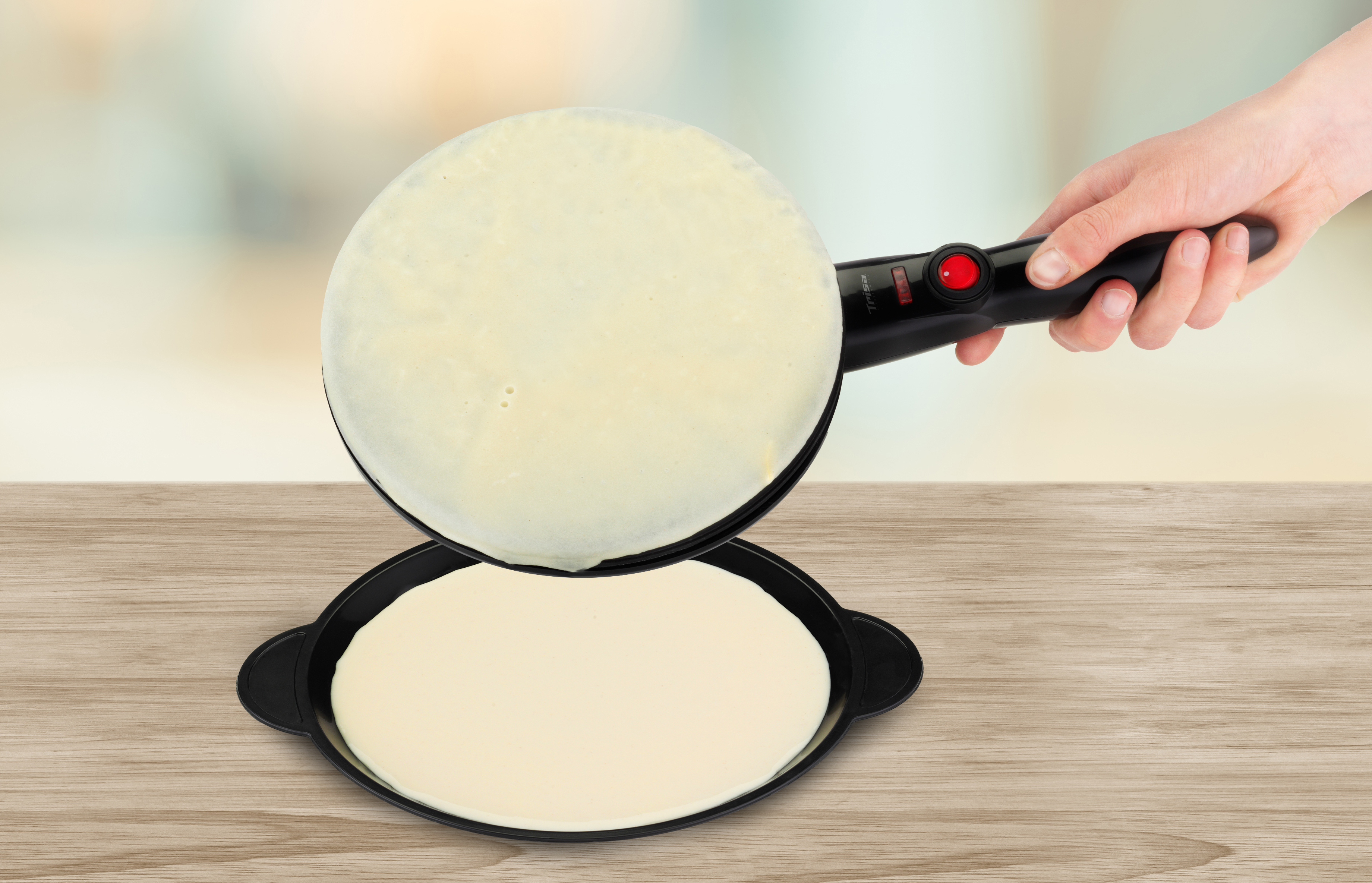 Schwarzer Crêpes-Maker mit einer Hand, die einen Crêpe auf einer Holzoberfläche wendet.