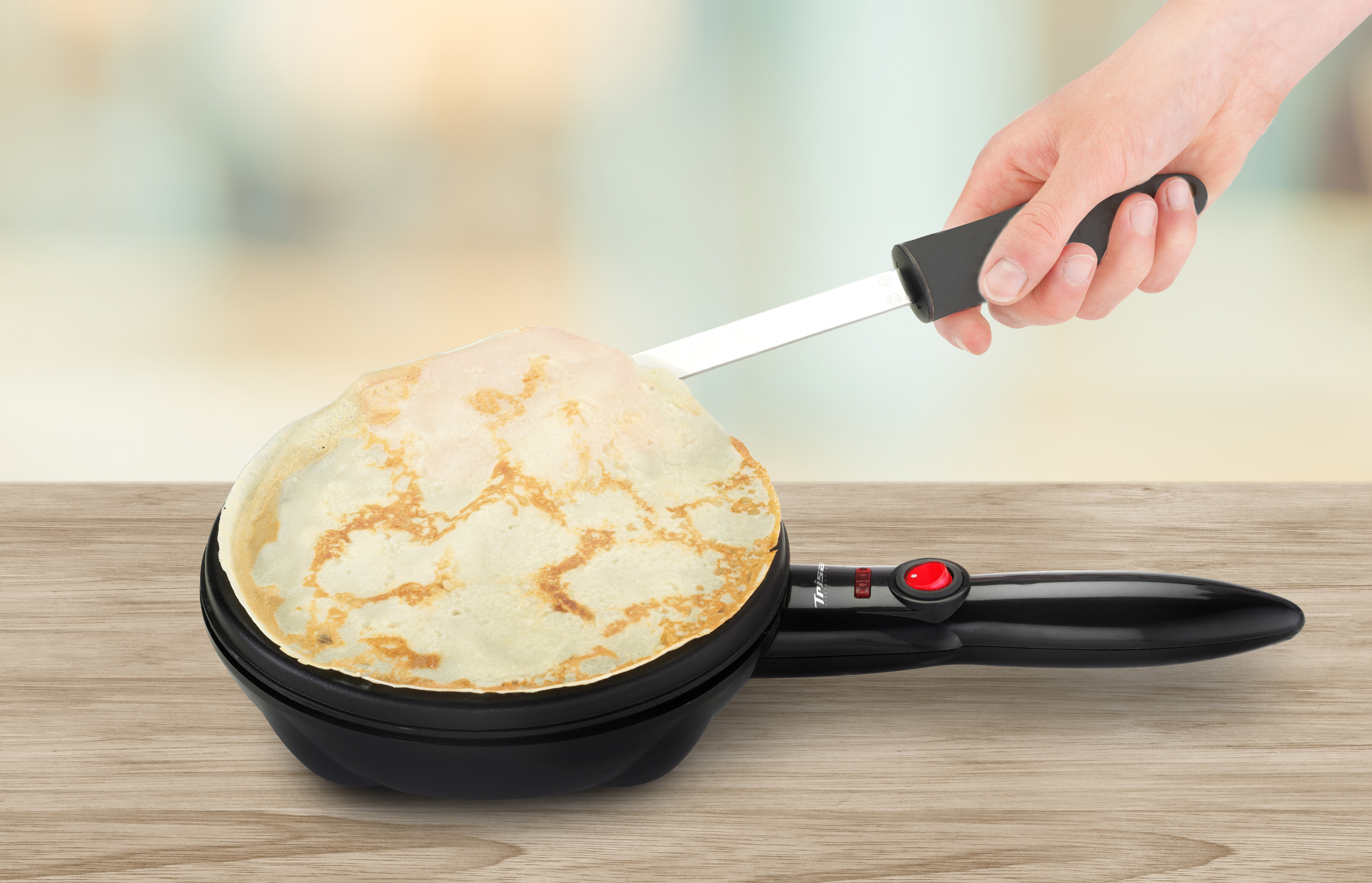 Crêpe-Maker mit einer Crêpe, die mit einem Spatel angehoben wird, auf Holz.