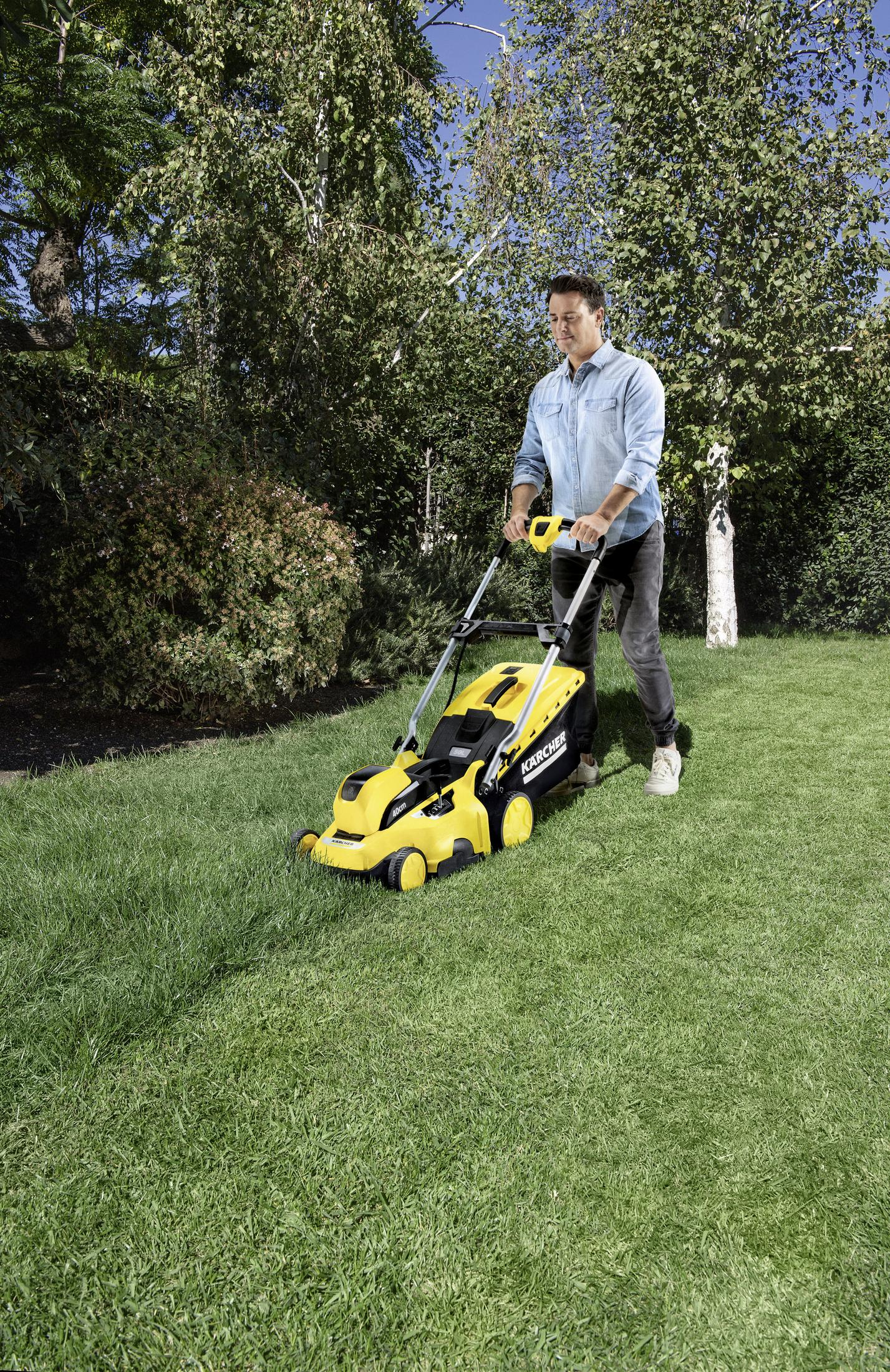 Un hombre cortando el césped con un cortacésped Kärcher amarillo y negro en un césped de hierba verde.