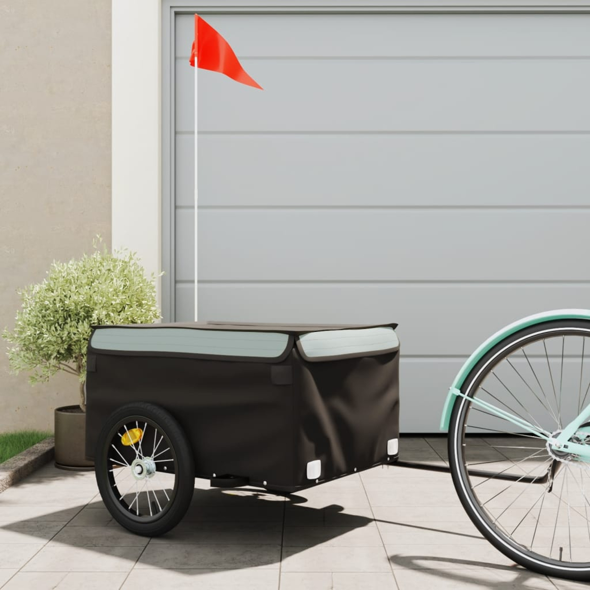 Ein Fahrradanhänger mit roter Fahne. Der Anhänger ist schwarz, das Fahrrad rechts.