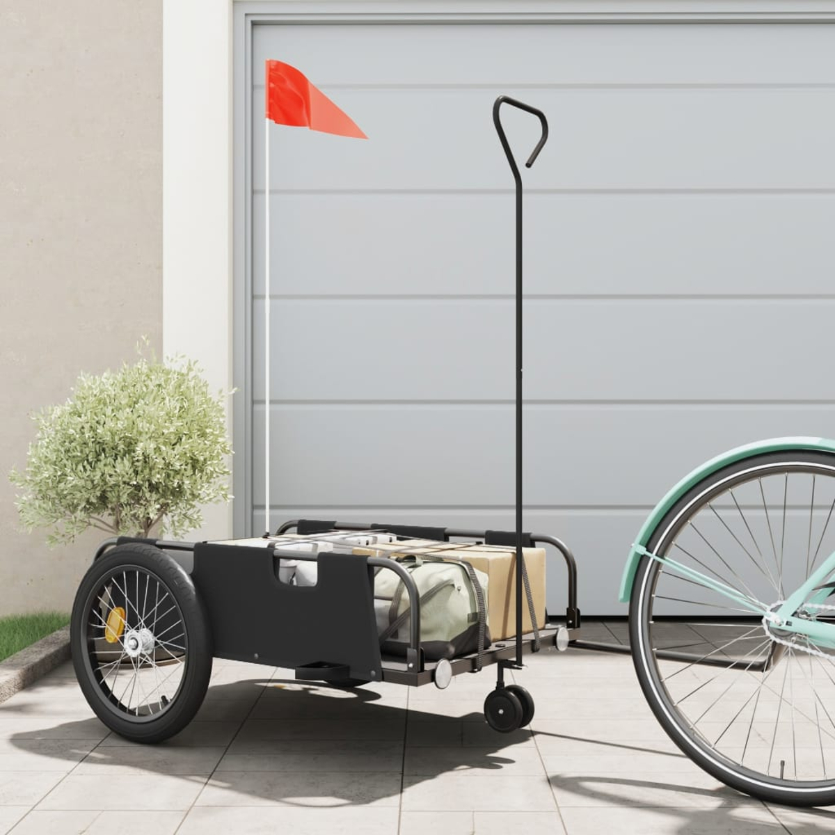 Ein Fahrradanhänger mit schwarzer Box und roter Fahne. Ein Fahrrad ist rechts.