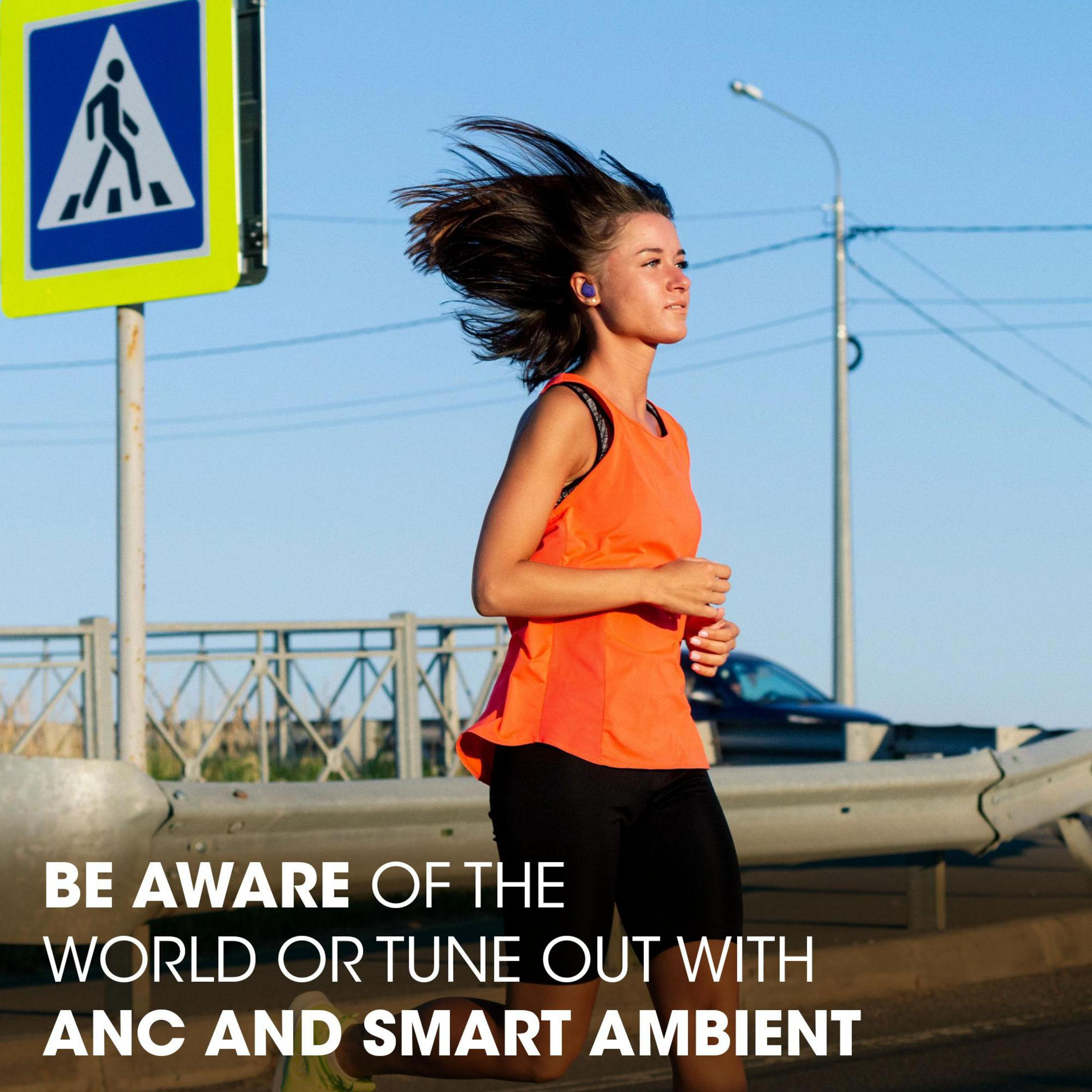 Kobieta biegnąca w pomarańczowym topie, czarnych szortach, ze słuchawkami w słoneczny dzień. Widoczny znak przejścia dla pieszych.