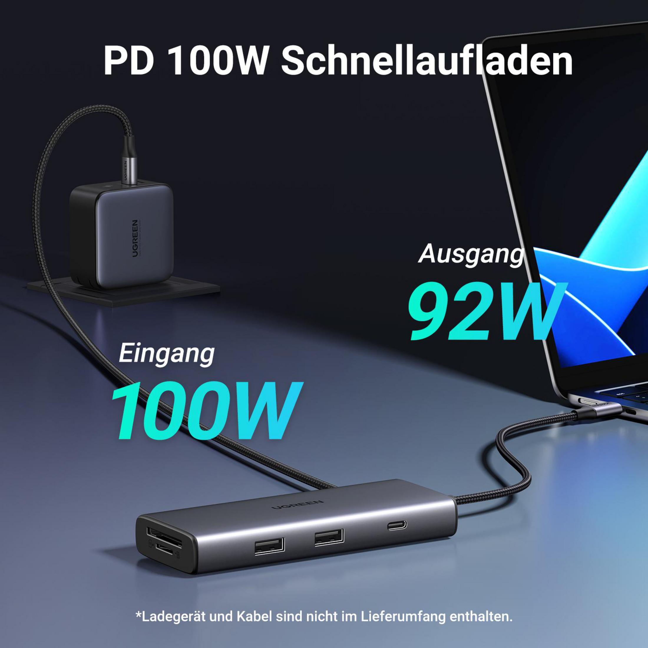 Adattatore di alimentazione e hub neri e grigi con cavi. Ha un ingresso da 100 W e un'uscita da 92 W. Laptop a destra.