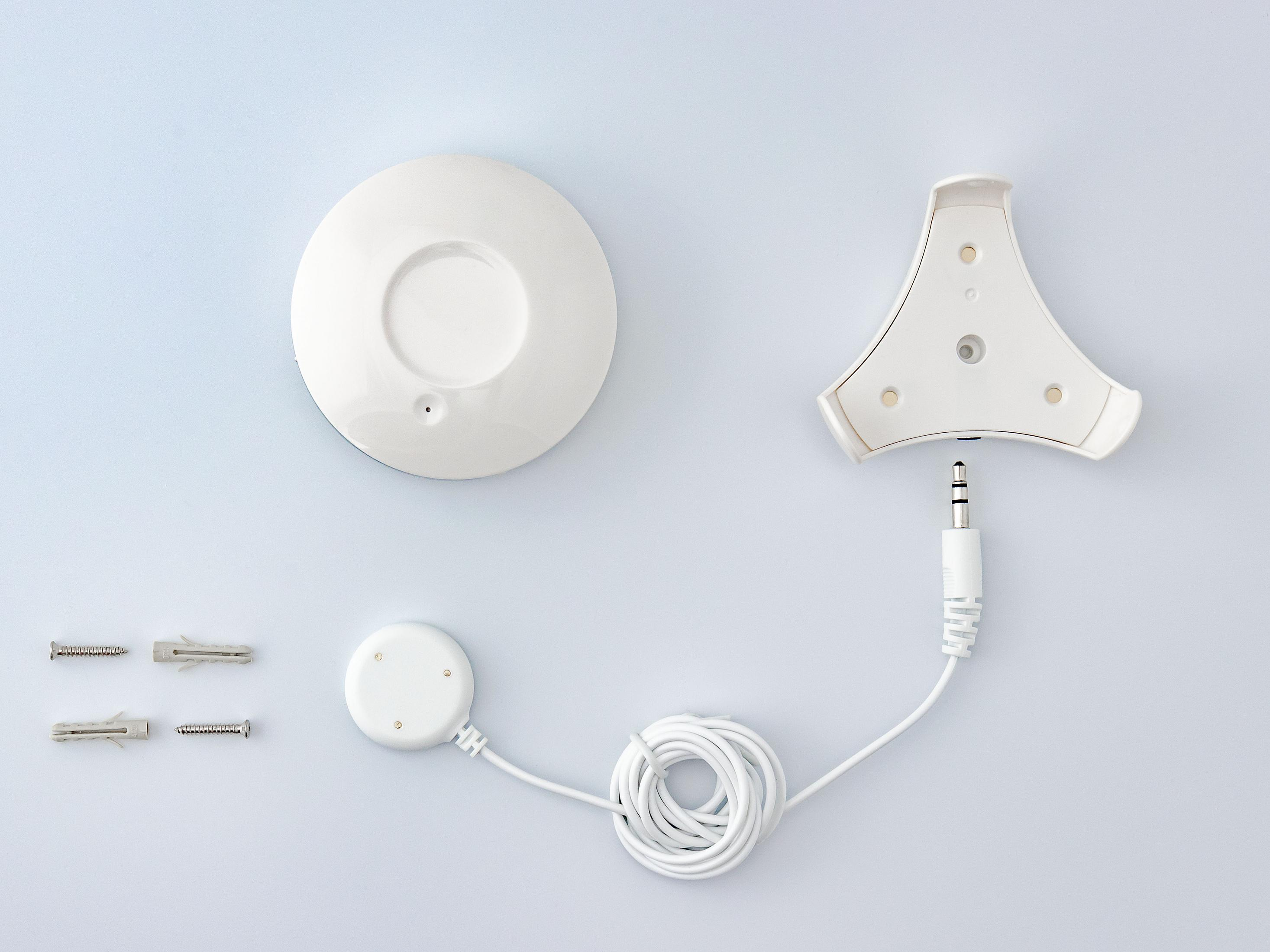 Weiße Gerätekomponenten. Runder Sensor, Halterung und Stecker. Weißer Hintergrund, einfache Anordnung.