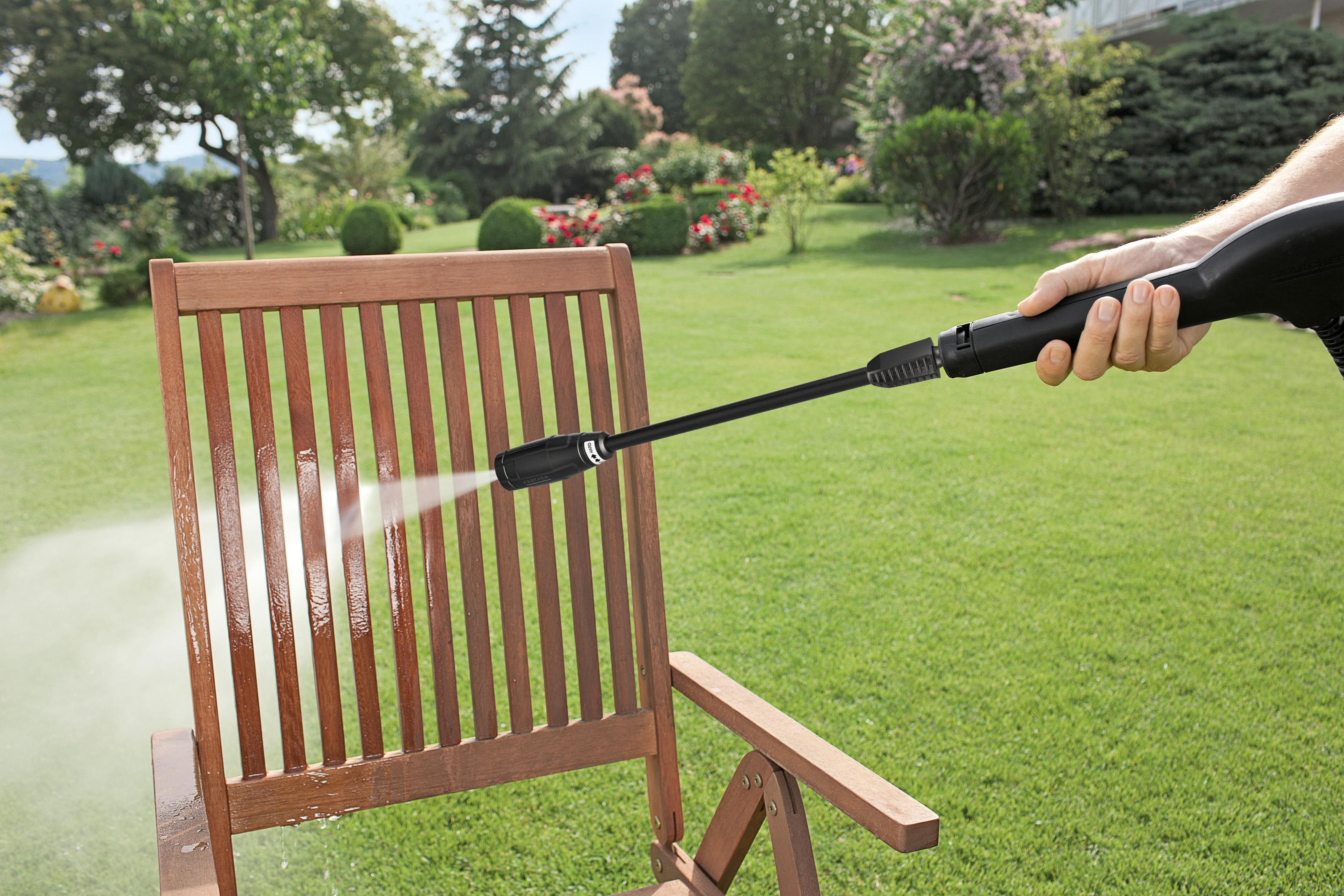 Een persoon die een houten stoel besproeit met een hogedrukreiniger in een tuin.